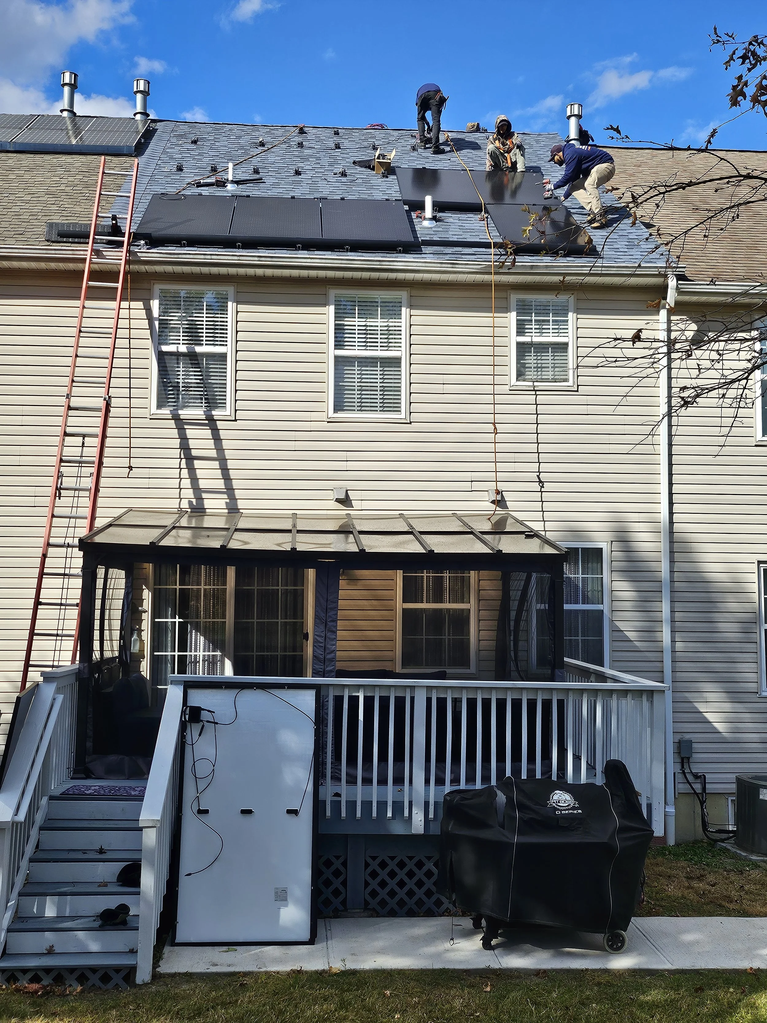 Crew installing solar panels on the roof of a NJ townhouse under clear skies. Equipment and safety ladders visible, showing the active solar installation process and commitment to clean energy upgrades.