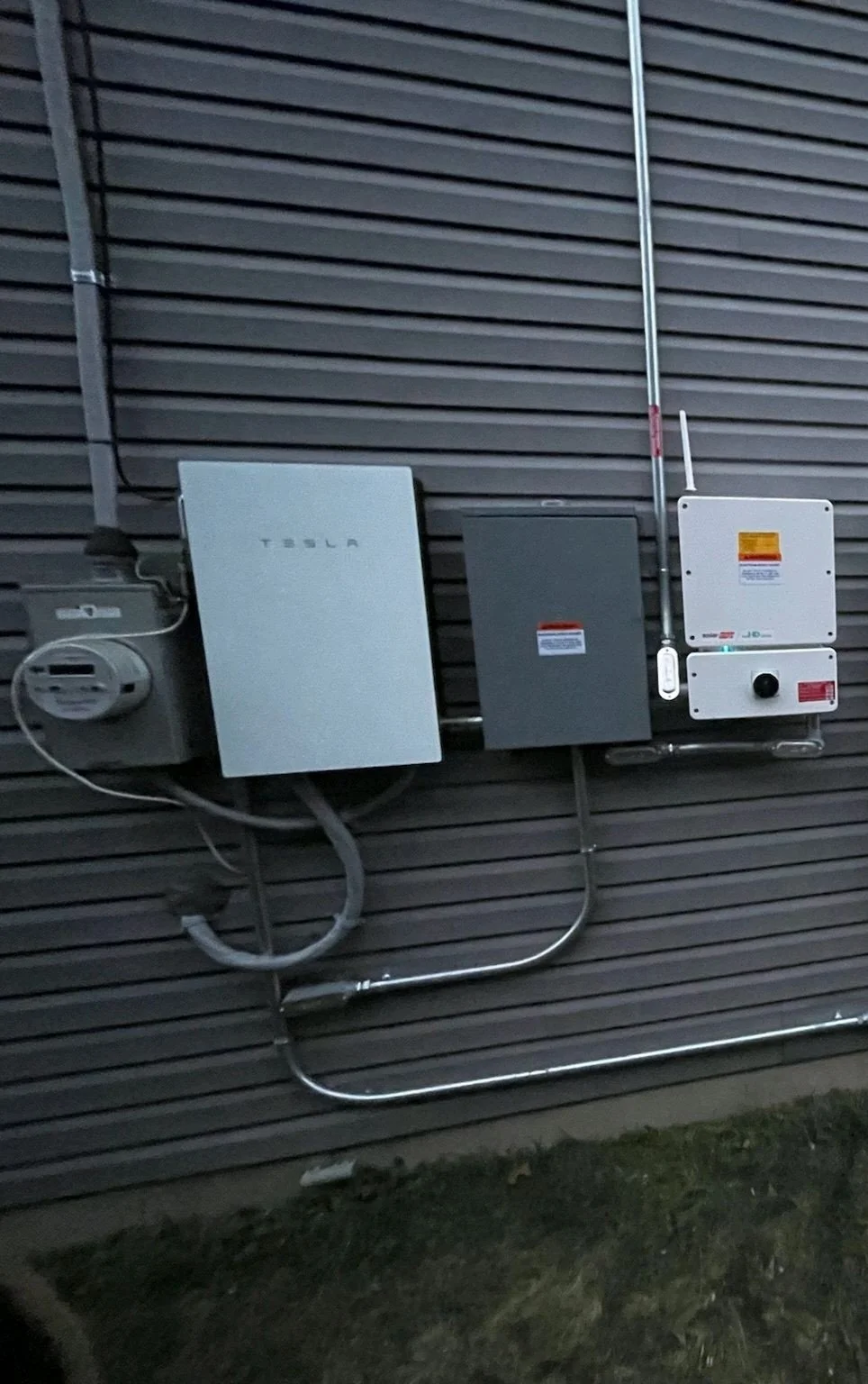 Tesla Powerwall battery and SolarEdge inverter installed on the exterior of a dark-paneled home in New Jersey, showcasing a complete solar plus storage setup at dusk.