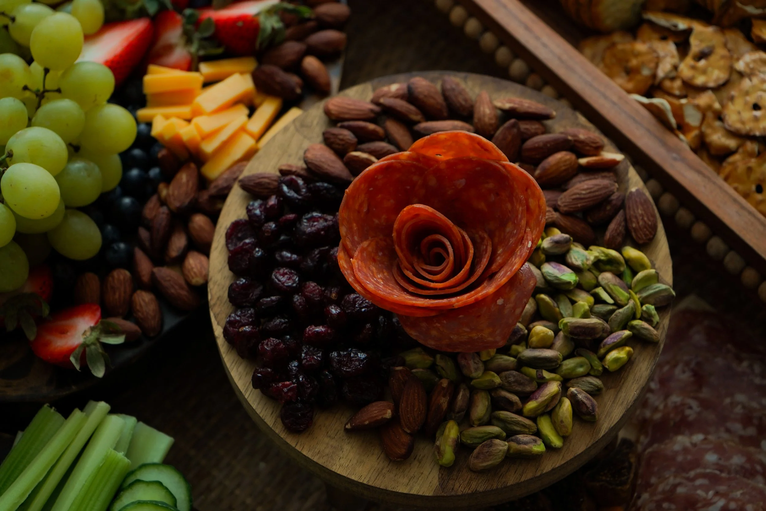 A cheese and charcuterie platter with grapes, dried fruits, nuts, and sliced vegetables.