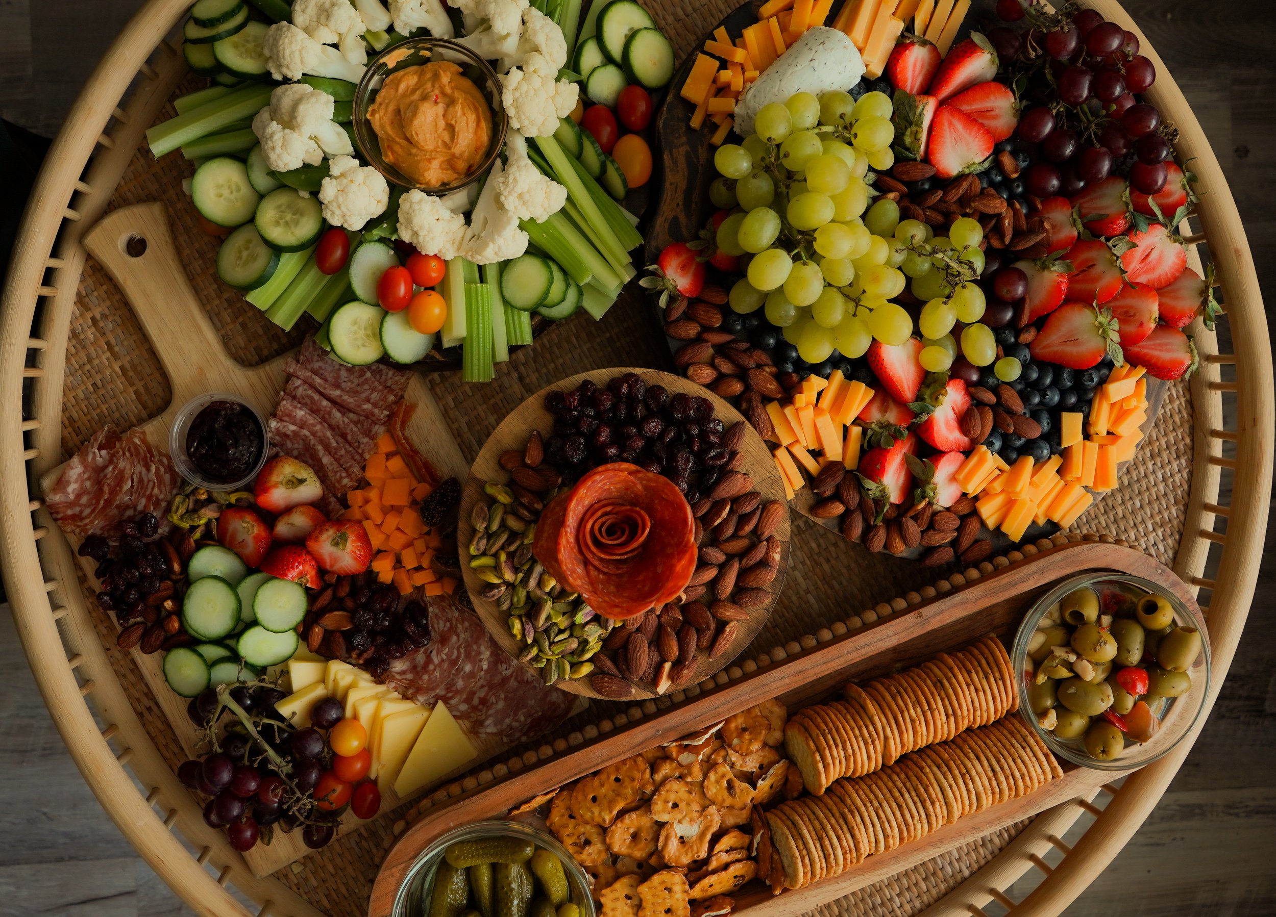 A large round tray filled with assorted fresh vegetables, fruits, cheeses, nuts, crackers, and dips arranged for a snack platter.