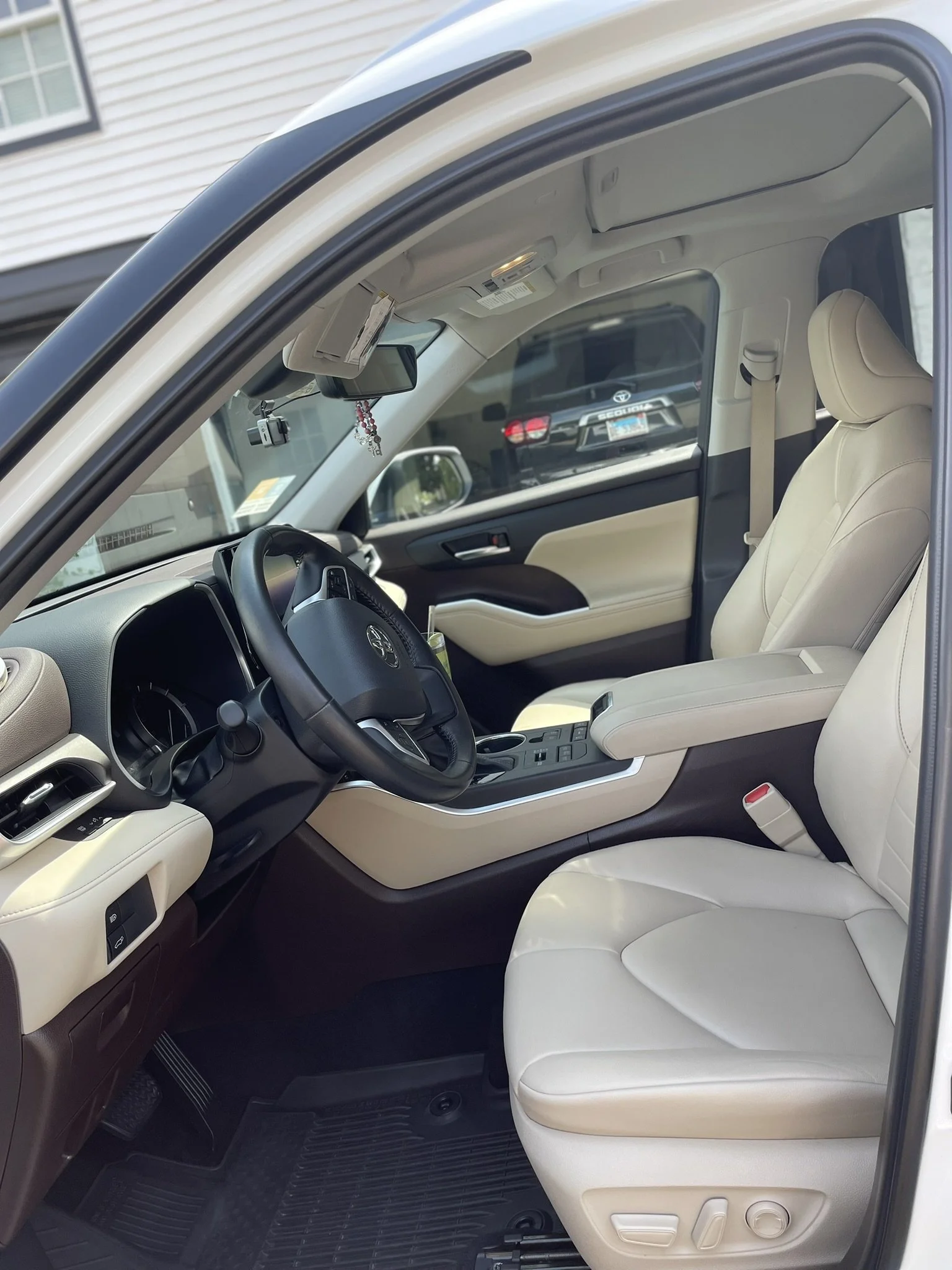 The image shows the interior of a vehicle with beige seats, a black steering wheel, and a center console, with a view of the driver's side door and part of the dashboard.
