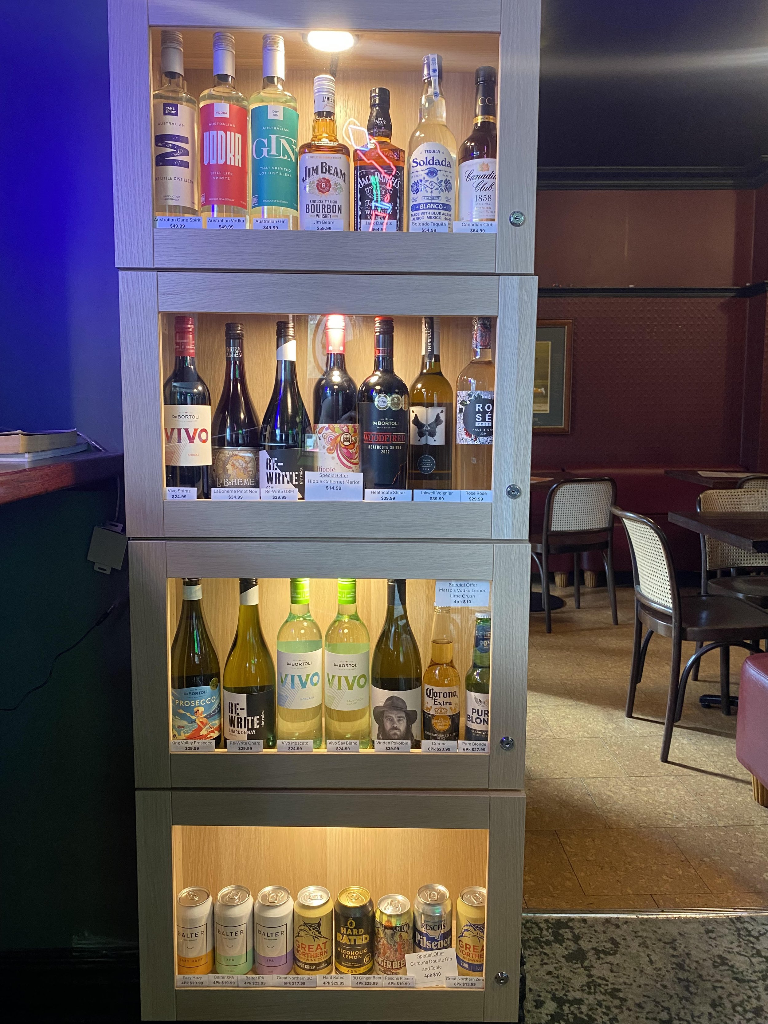 A bar counter with a variety of craft beer taps, including labels for Great Northern, 4 Pines Lager, Draught, Hawkers Pale Ale, and others, with a blurred background featuring a person in a blue hoodie.