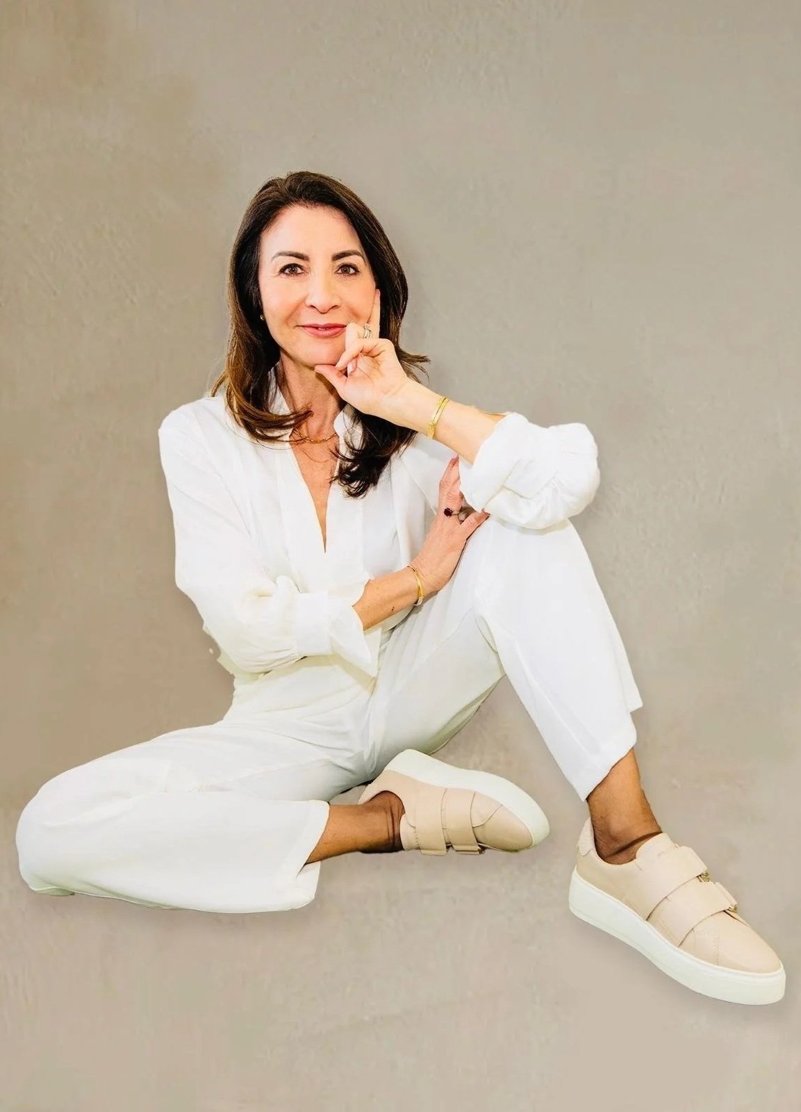 Naomi Nahoum, beauty business coach, sitting cross-legged and smiling in relaxed portrait.