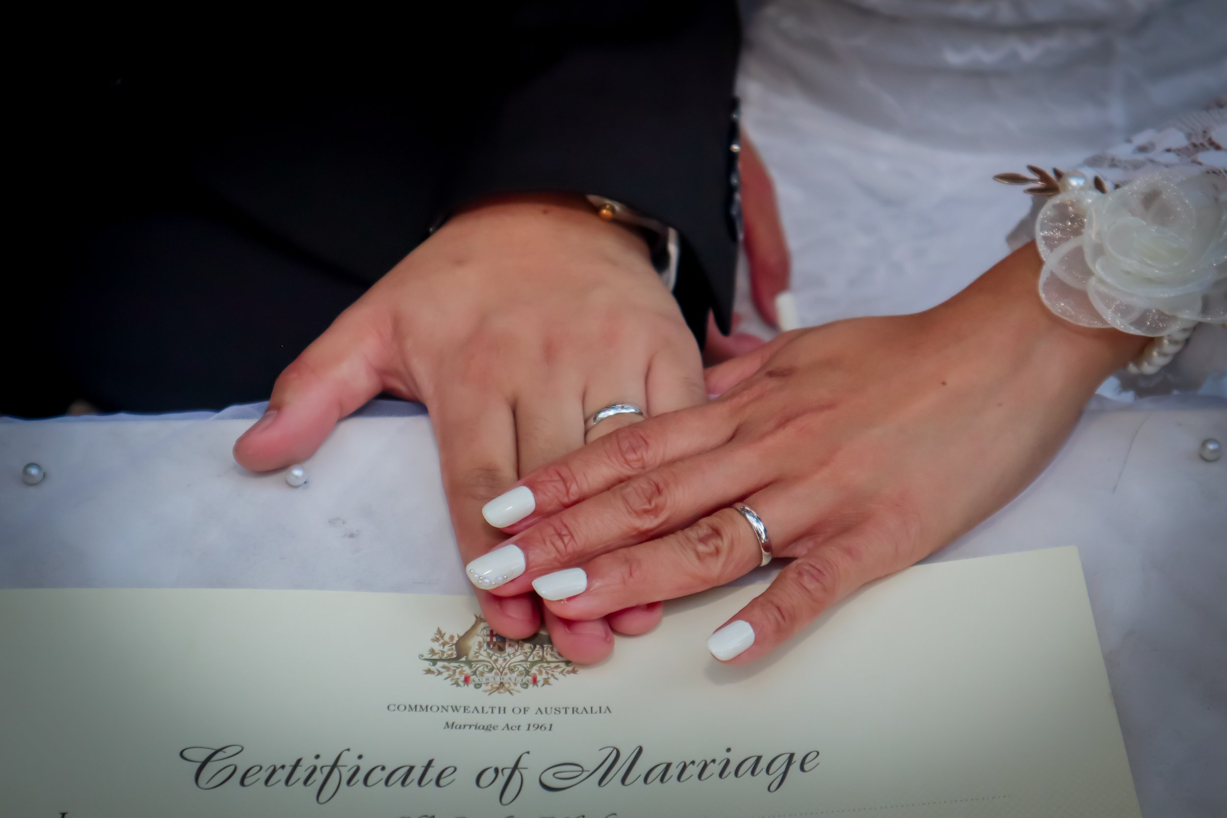 Close-up of a newlywed couple's hands with wedding rings, resting on a marriage certificate from Australia.