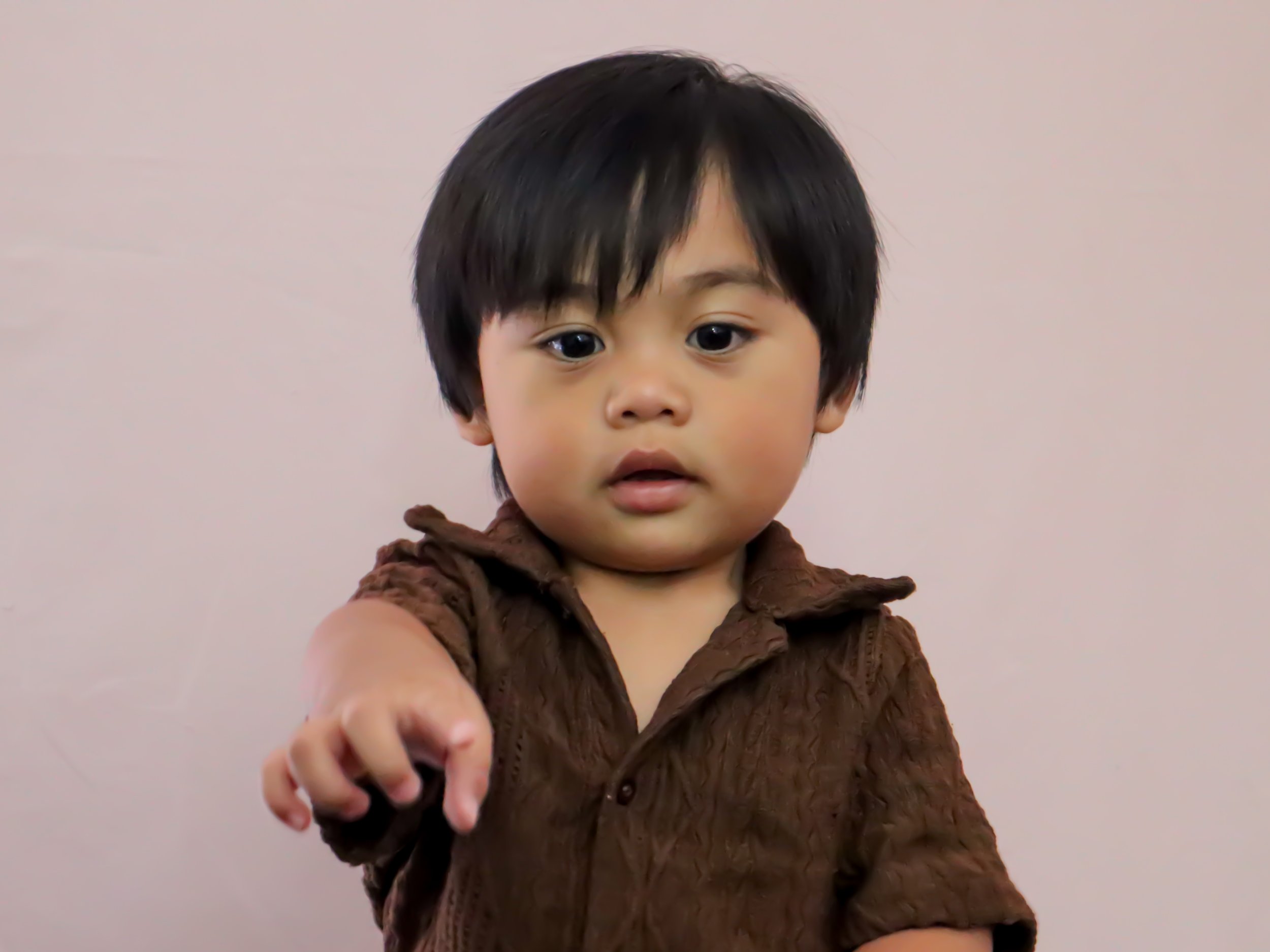 A young boy with black hair and a brown shirt extending his hand forward with a focused expression.