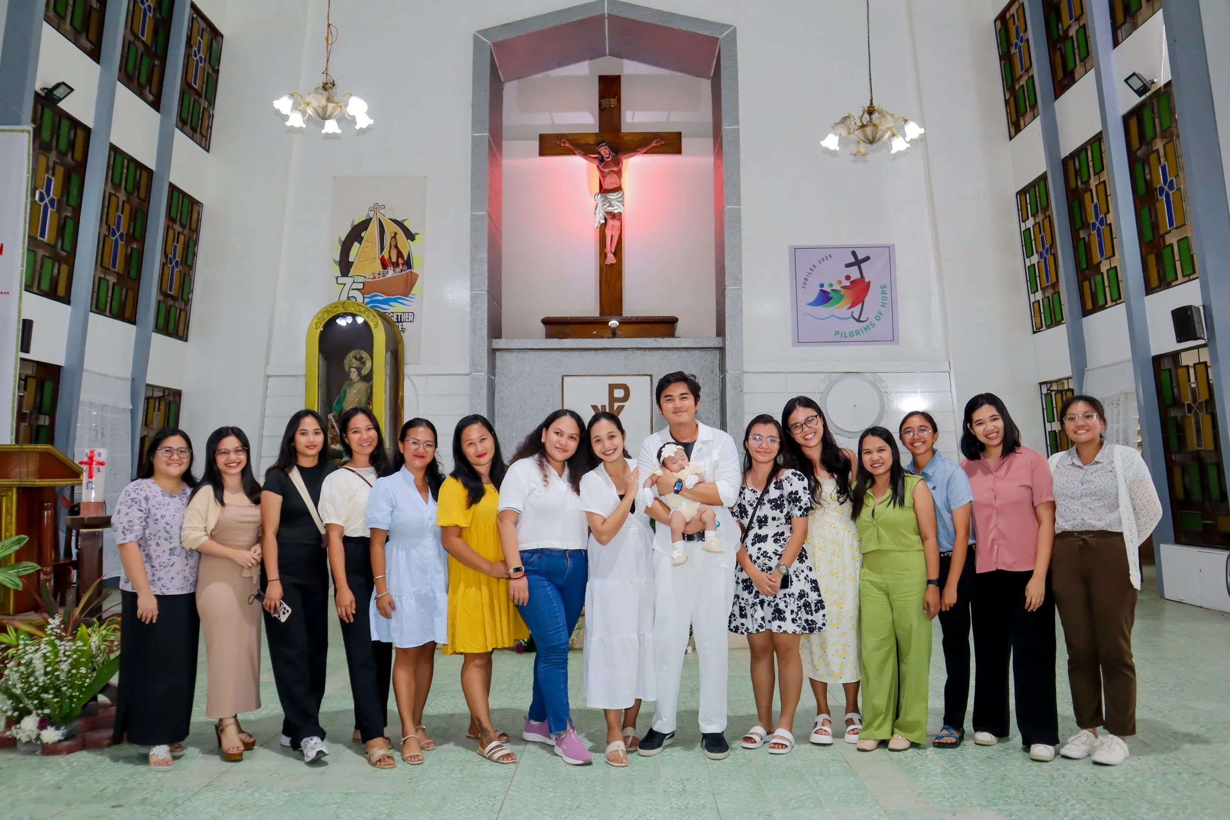 Group of people standing inside a church in front of an altar with a crucifix, a statue, and colorful banners, smiling for the photo.