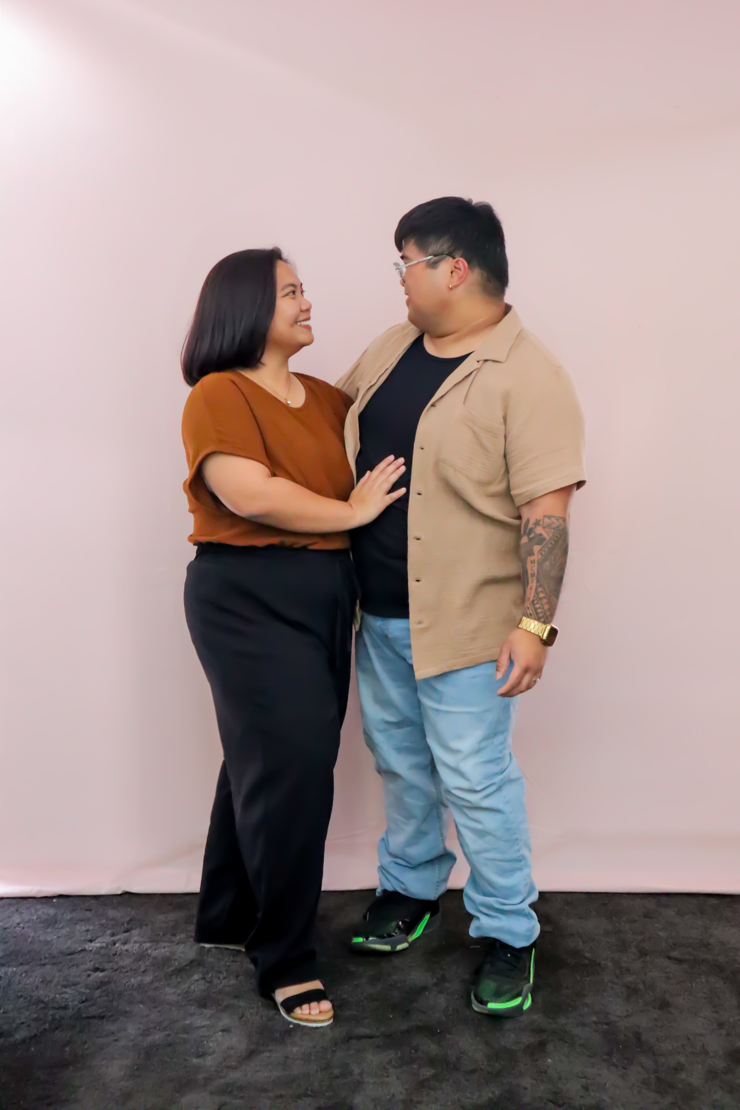 A couple standing close together, gazing into each other's eyes, with a pink backdrop.