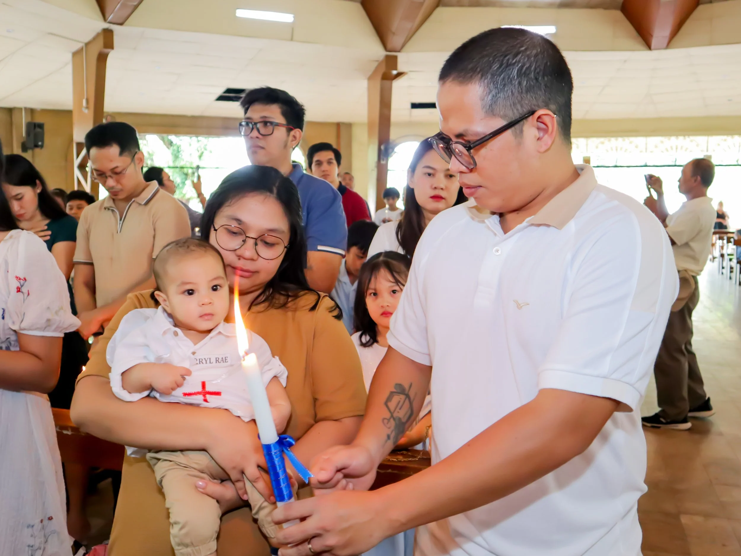 A family lighting a candle during a religious ceremony surrounded by other attendees in a church or chapel.