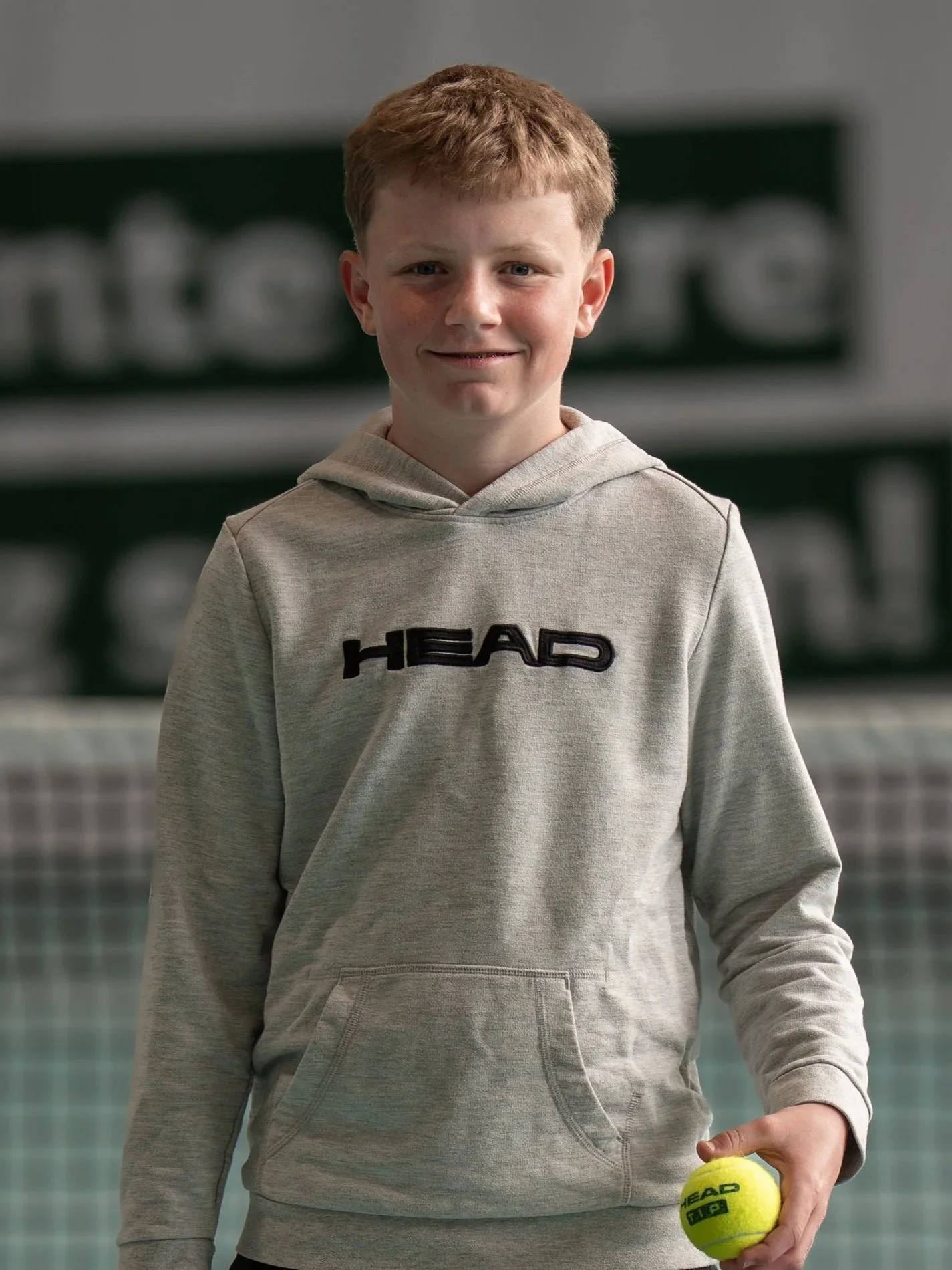 Ein Junge hält einen Tennisball in der Hand und steht in einer Tennishalle.