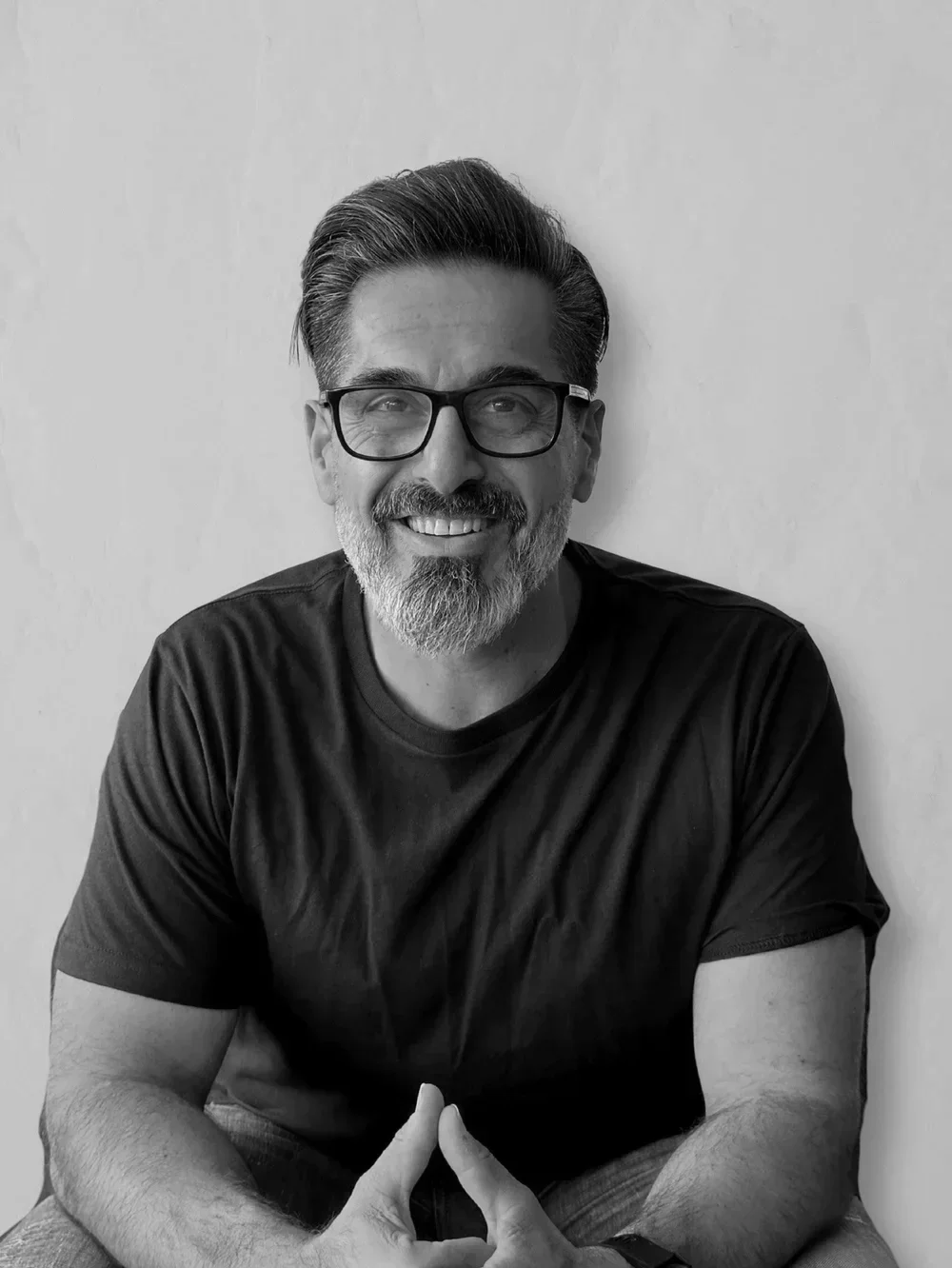 Black and white photo of a man smiling, wearing a light-colored sport coat and a white shirt, with people in the background at a social event.