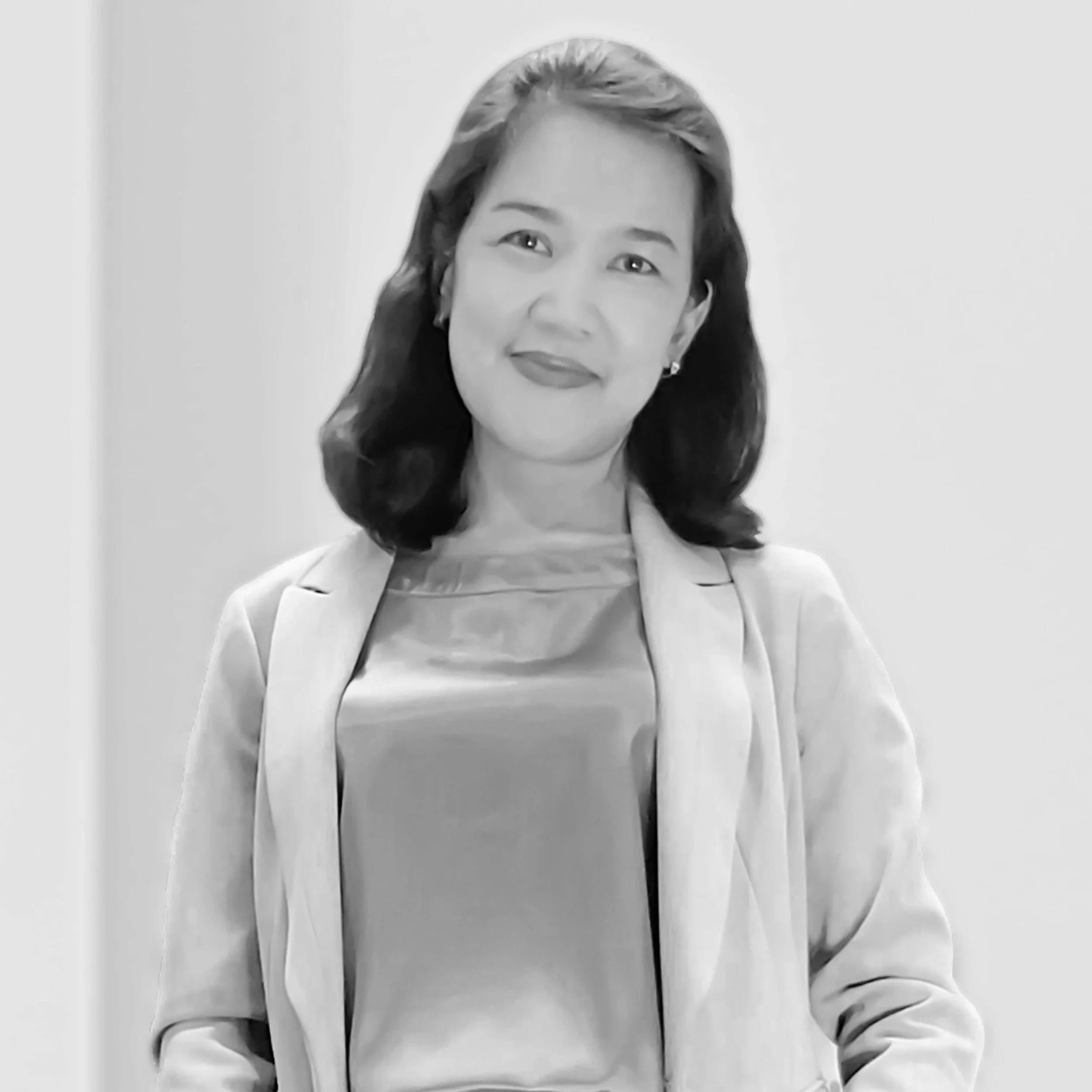 Black and white photo of a woman with dark shoulder-length hair, wearing a blazer over a satin top, smiling softly at the camera.