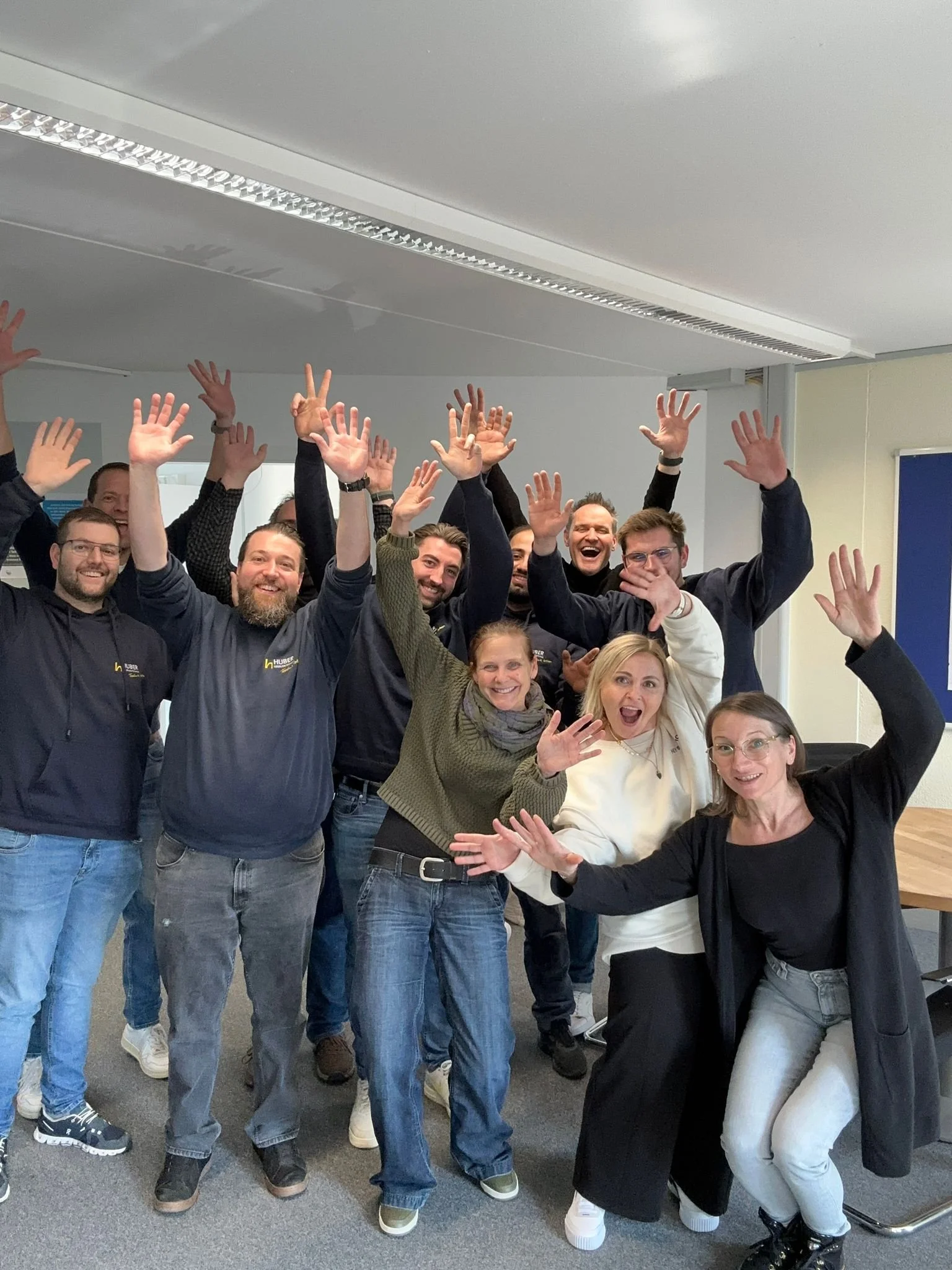 Gruppe lachender Menschen in einem Büro, die jubeln und die Hände hochheben.