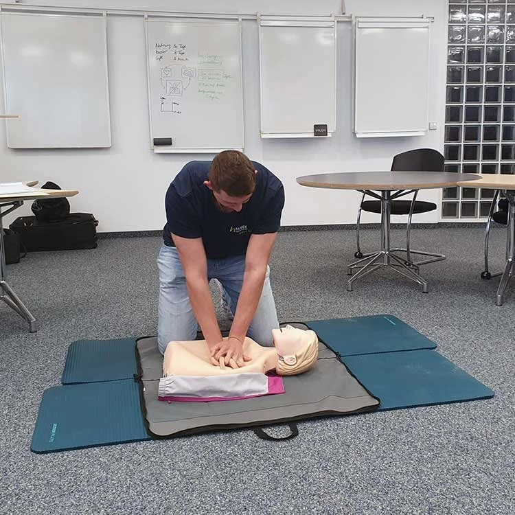 Person übt Herzdruckmassage auf eine Übungspuppe in einem Schulungsraum.