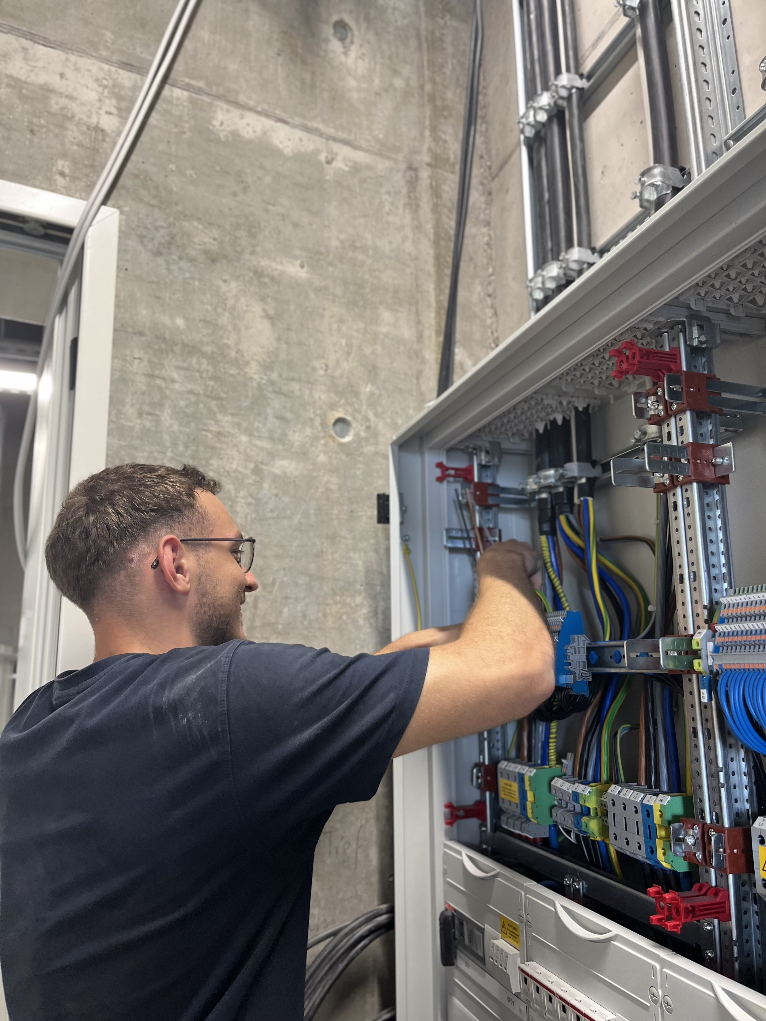 Ein Mann arbeitet an einem offenen Schaltschrank mit vielen Kabeln und elektrischen Komponenten.