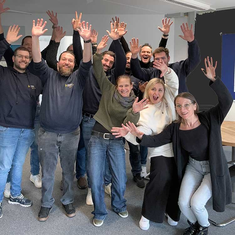 Eine Gruppe von Menschen, die fröhlich in einem Raum feiern und in die Kamera winken.