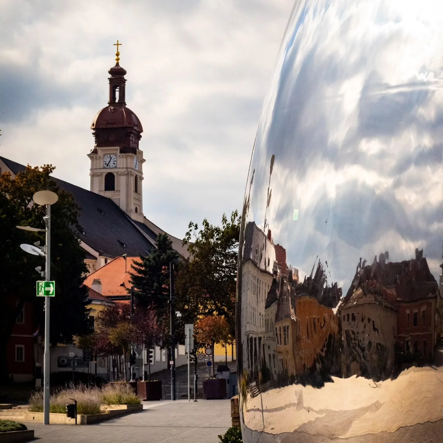 Is it an illusion? It certainly looks like one.
Which one is your favourite?

What you&rsquo;re seeing is an incredible art installation in the heart of Győr, right by the river &mdash; a circular, lentil-shaped mirror that blends into the sky, the r