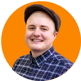 Young man with a broad smile wearing a checkered shirt and a brown cap, against an orange background.