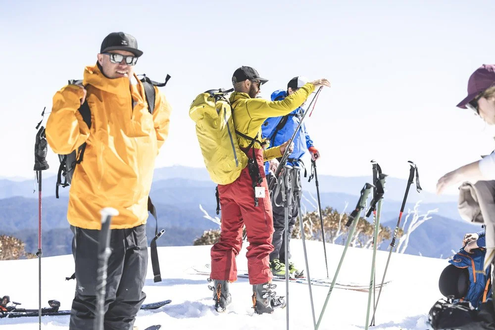 Group of skiers in colorful winter gear preparing on snowy mountain with mountain range in background at the Australian Backcountry Festival.