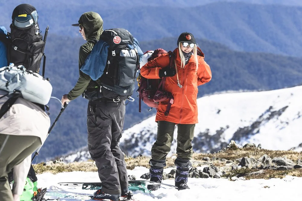A group of hikers on snow-covered terrain in the mountains, wearing winter gear and backpacks at the Australian Backcountry Festival.