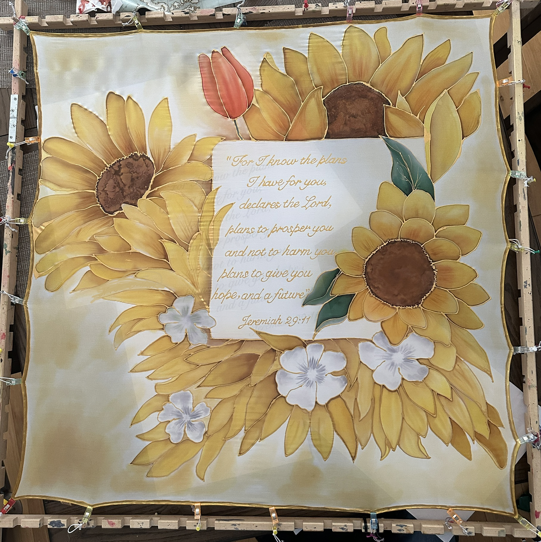 A decorative fabric with a sunflower design and a Bible quote from Jeremiah 29:11, surrounded by white flowers and green leaves.
