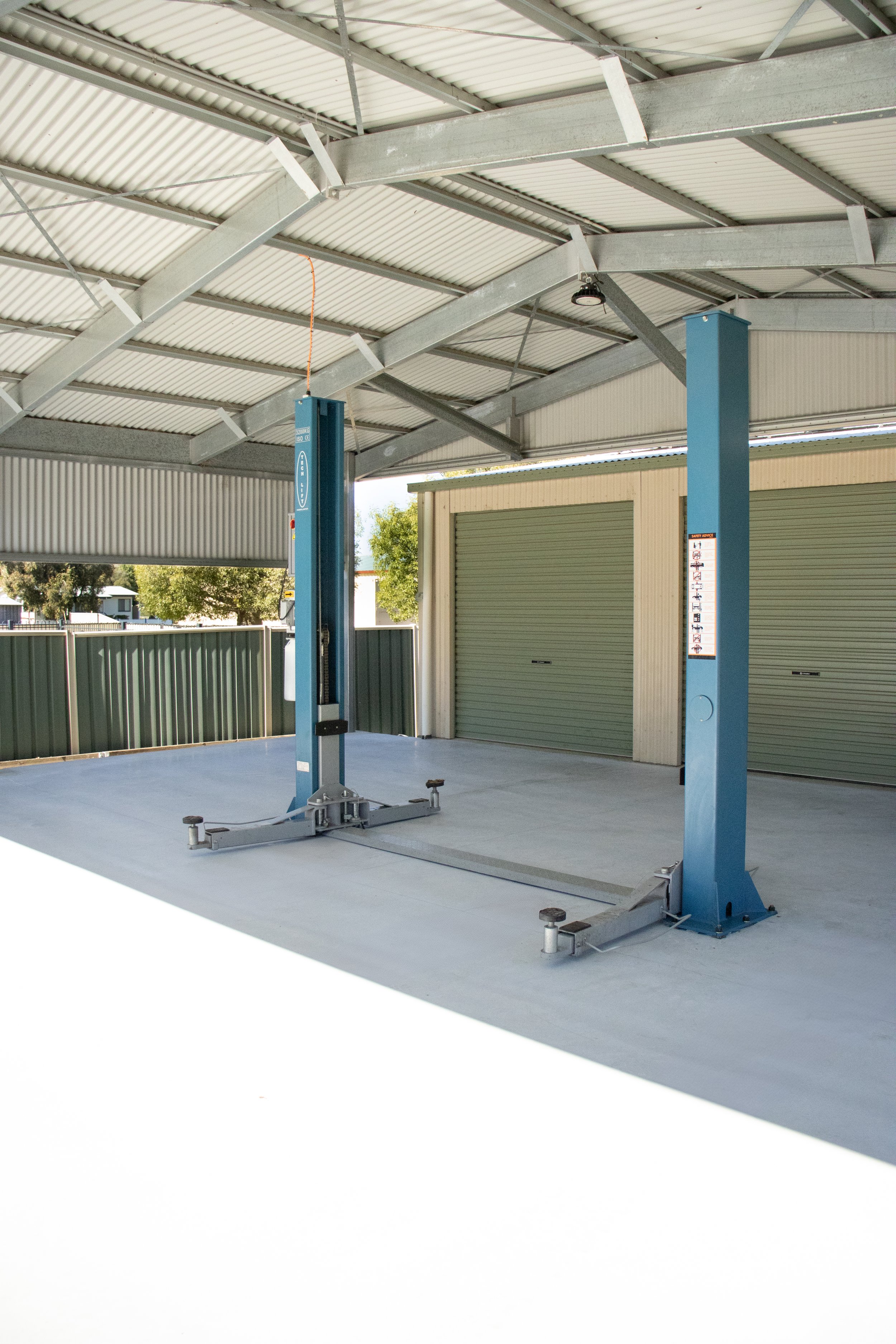 Vehicle hoist on concrete driveway under shed extension.
