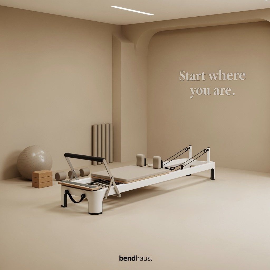 Minimalist exercise room with a Pilates reformer, exercise ball, foam rollers, and wooden blocks, with the phrase 'Start where you are.' on the wall.