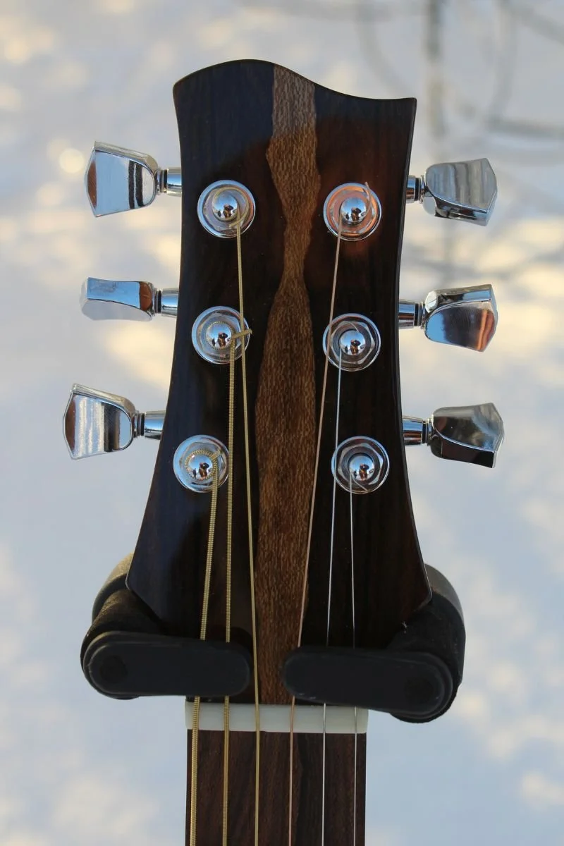 Close-up of the Snowbird guitar headstock, featuring a dark wood front with a contrasting center stripe and chrome tuners.
