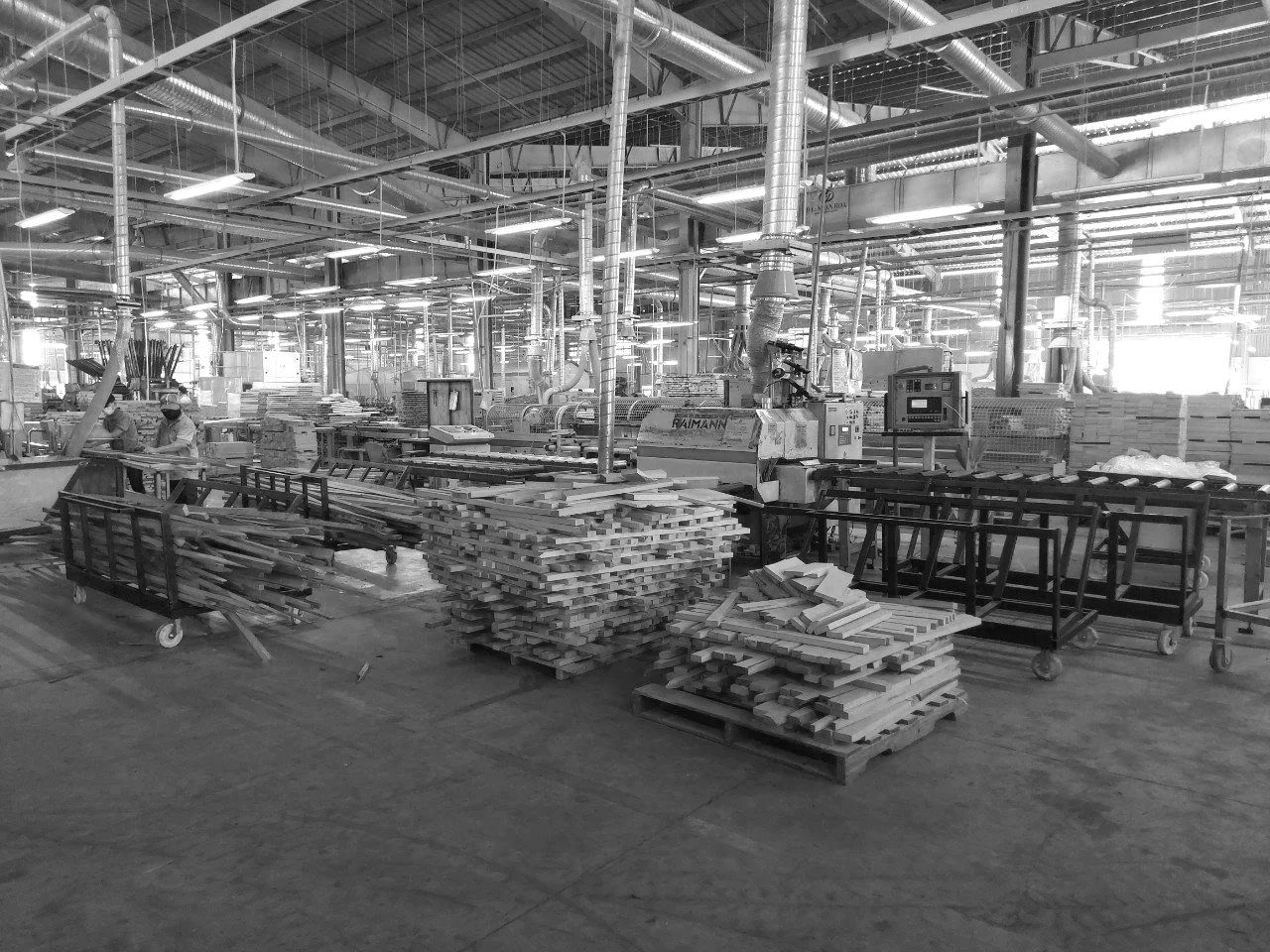 Industrial woodworking factory with stacks of wooden planks, machinery, and workers wearing masks.