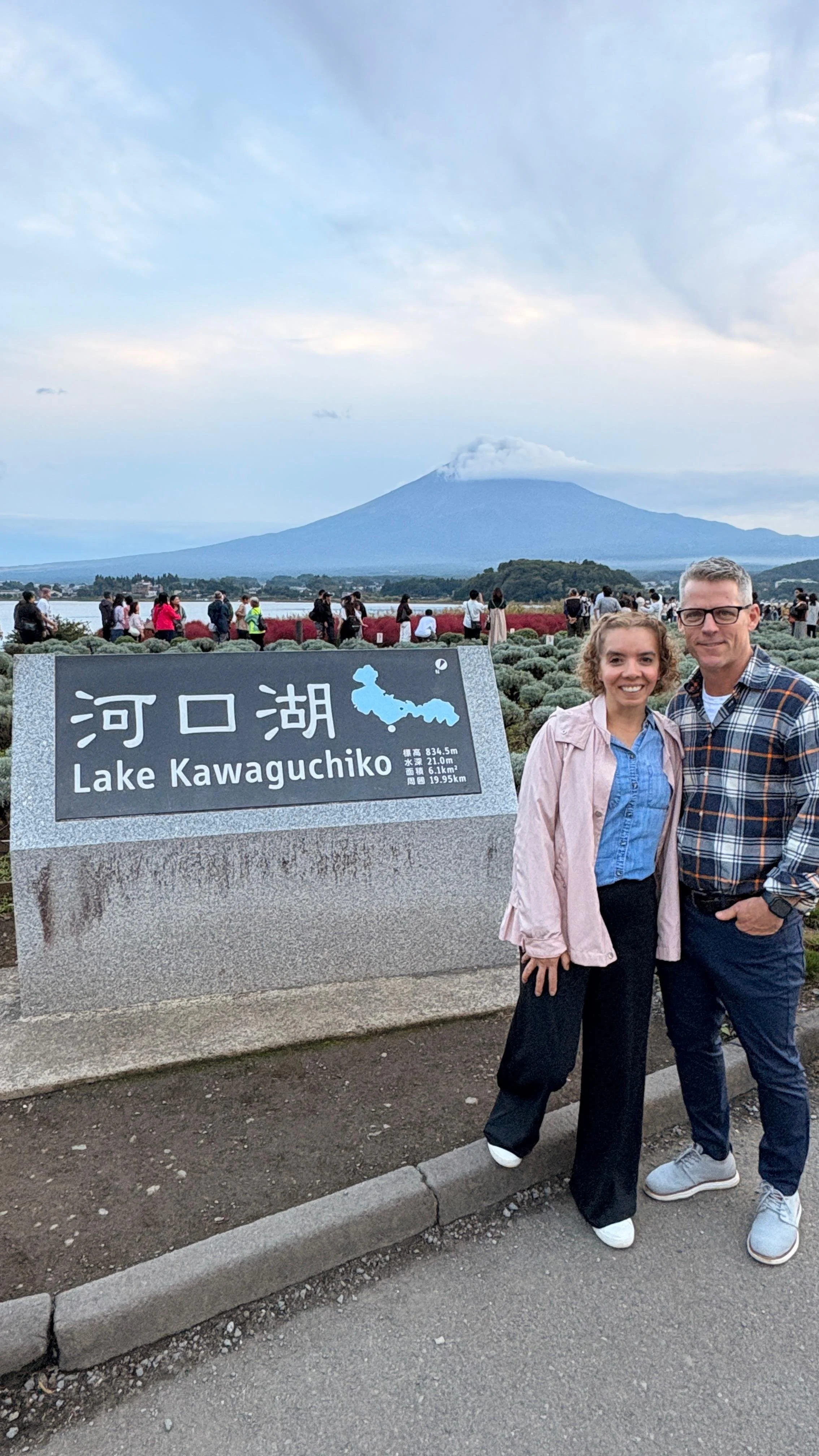 Two people posing in front of a sign for Lake Kawaguchiko with Mount Fuji in the background.