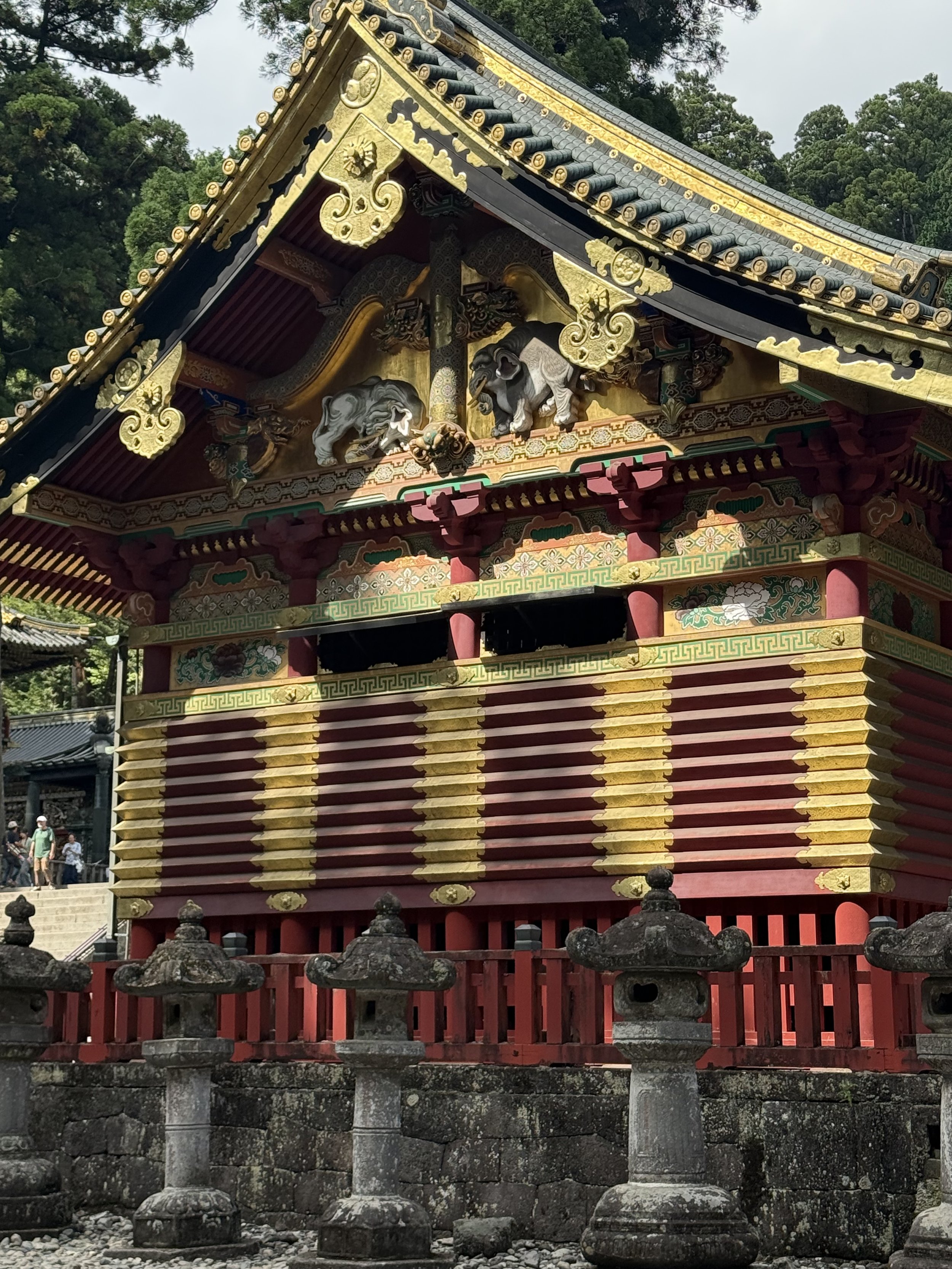 Traditional Japanese temple with ornate gold and red decorations, wooden lion sculptures, and stone lanterns in front.