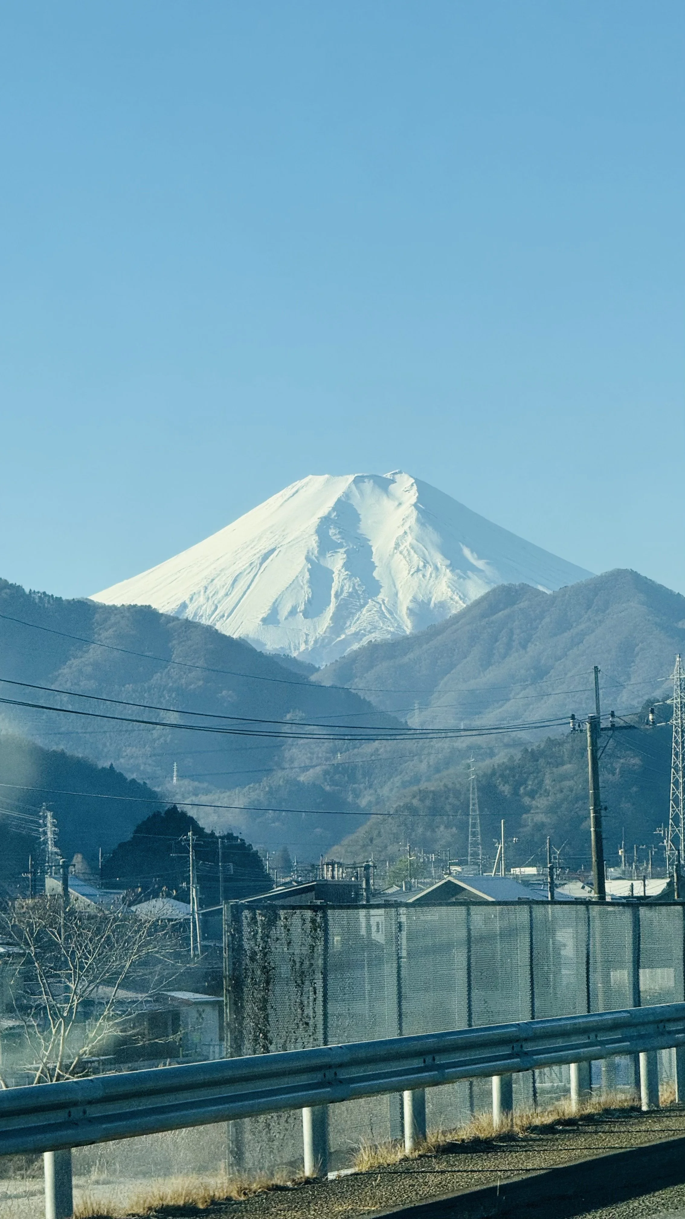 Snow-capped Mount Fuji visible over a suburban area with power lines, fences, and trees.