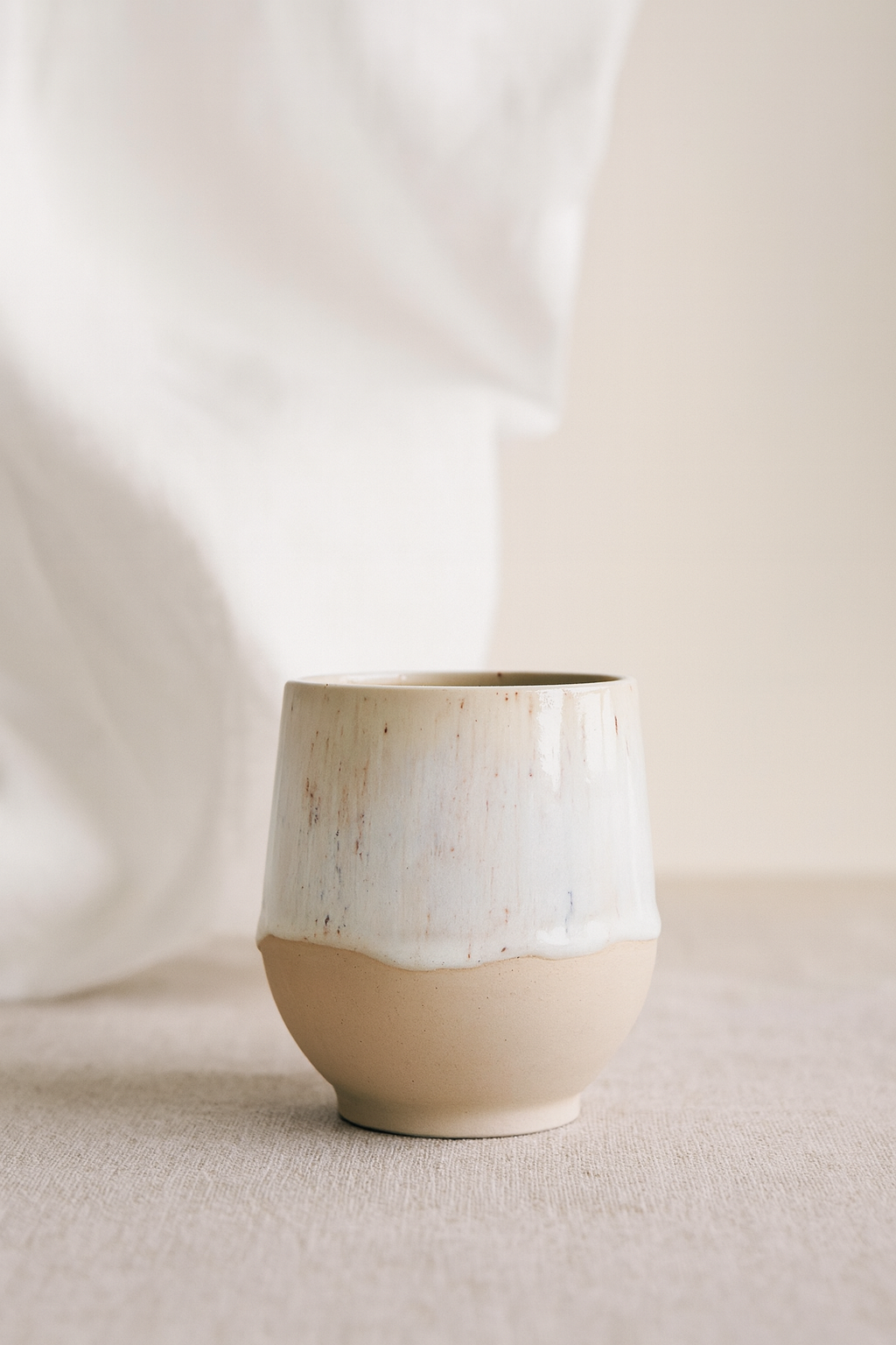 Tasse gobelet en céramique artisanale en argile blanche, émail beige et blanc, forme douce, fait main en Belgique.