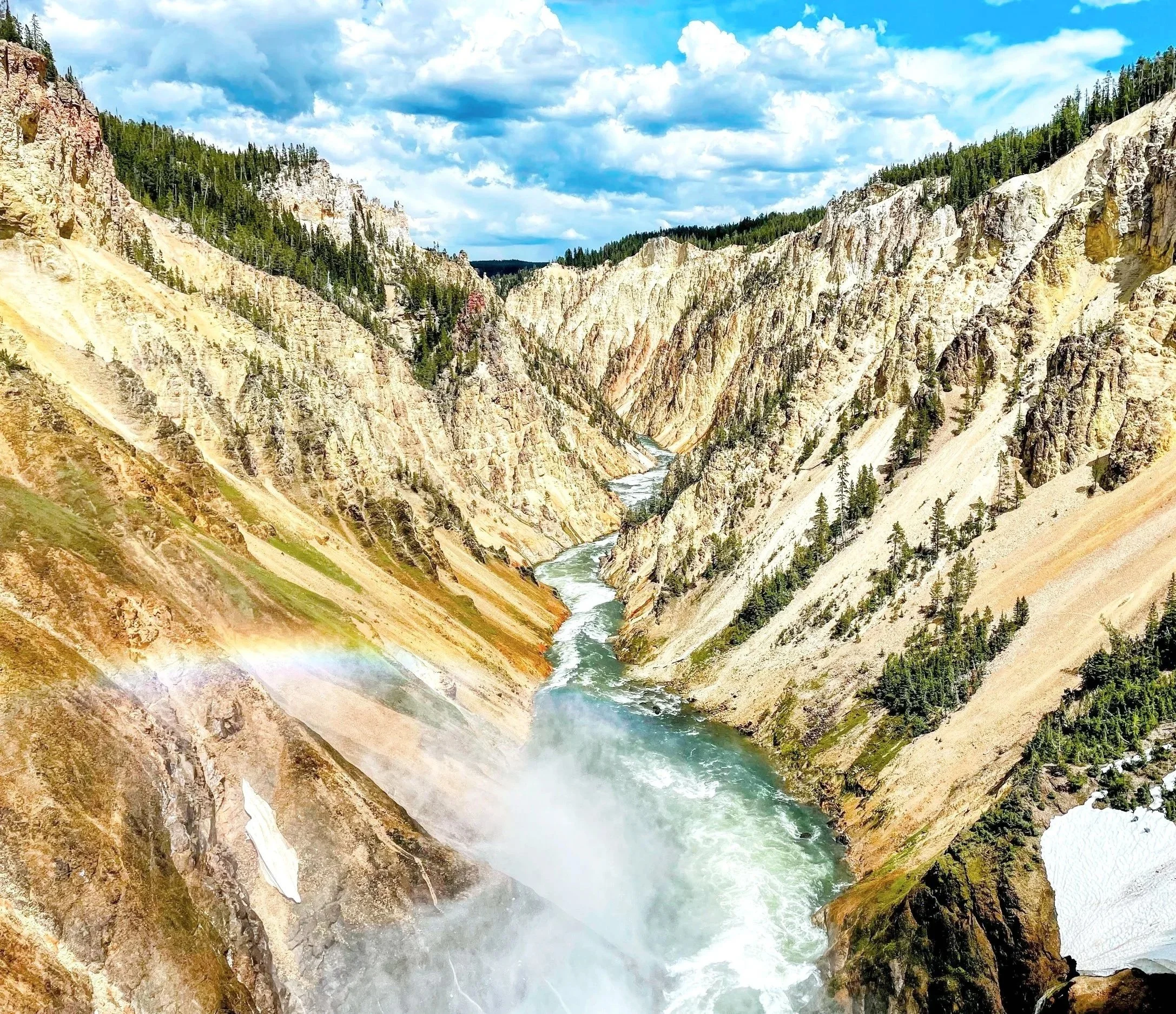 View of a canyon with a river flowing through, surrounded by steep cliffs covered in trees, under a partly cloudy sky.