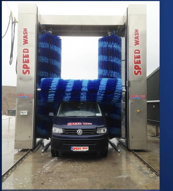 A car is in a car wash with large blue and dark blue spinning brushes surrounding it.