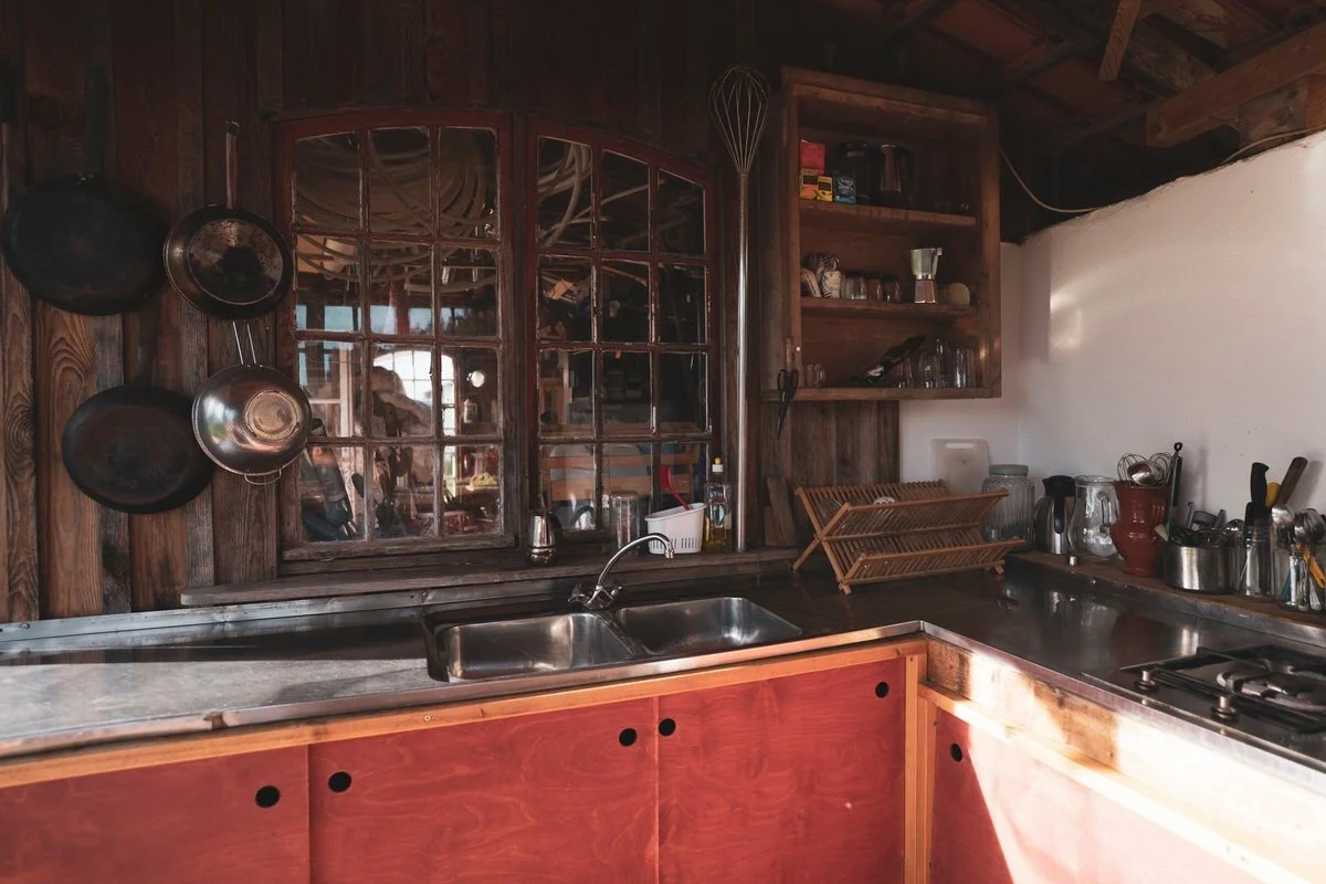 Kitchen with wooden cabinets, stainless steel sink, hanging pans, and various kitchen utensils and appliances on the countertop.