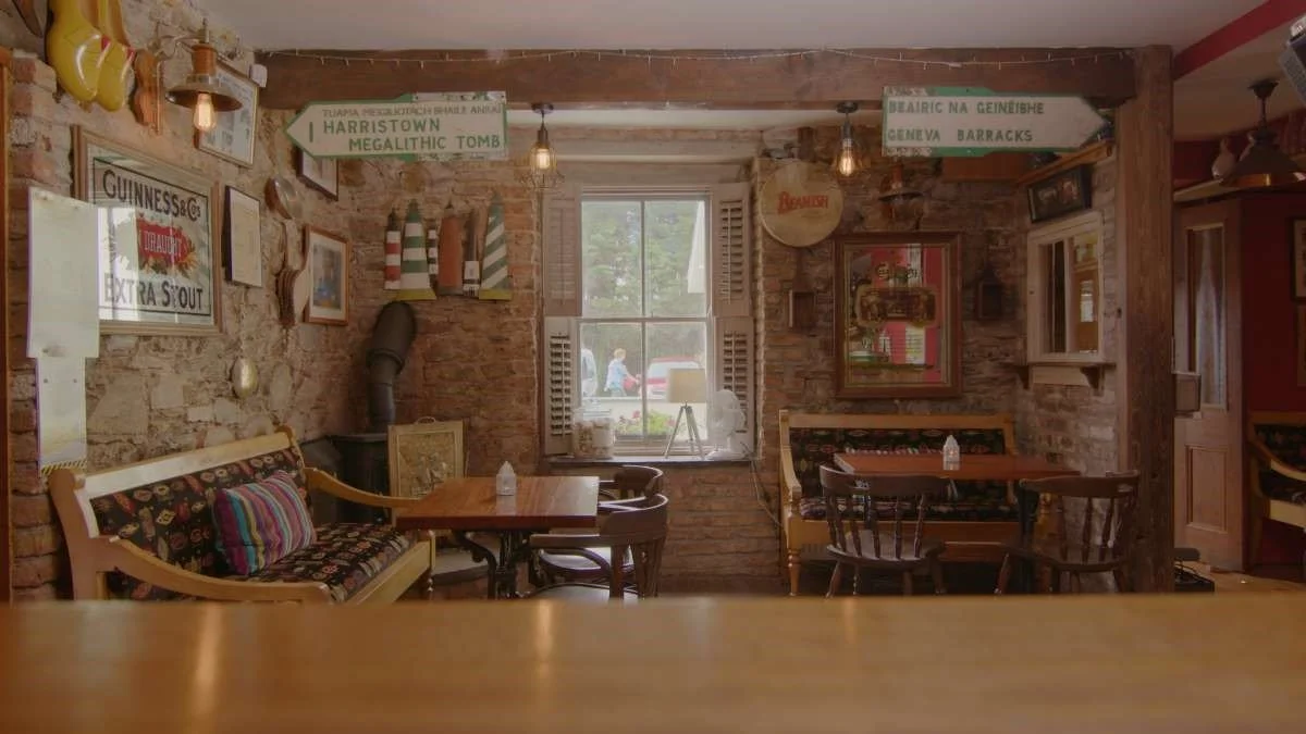 Interior of a cozy rustic restaurant with brick walls, wooden furniture, and vintage decor, featuring signs and framed pictures on the walls and a window with open shutters letting in natural light.