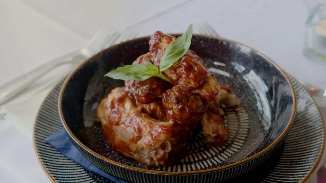 A black and gold bowl with pieces of meat covered in barbecue sauce and garnished with a basil leaf.