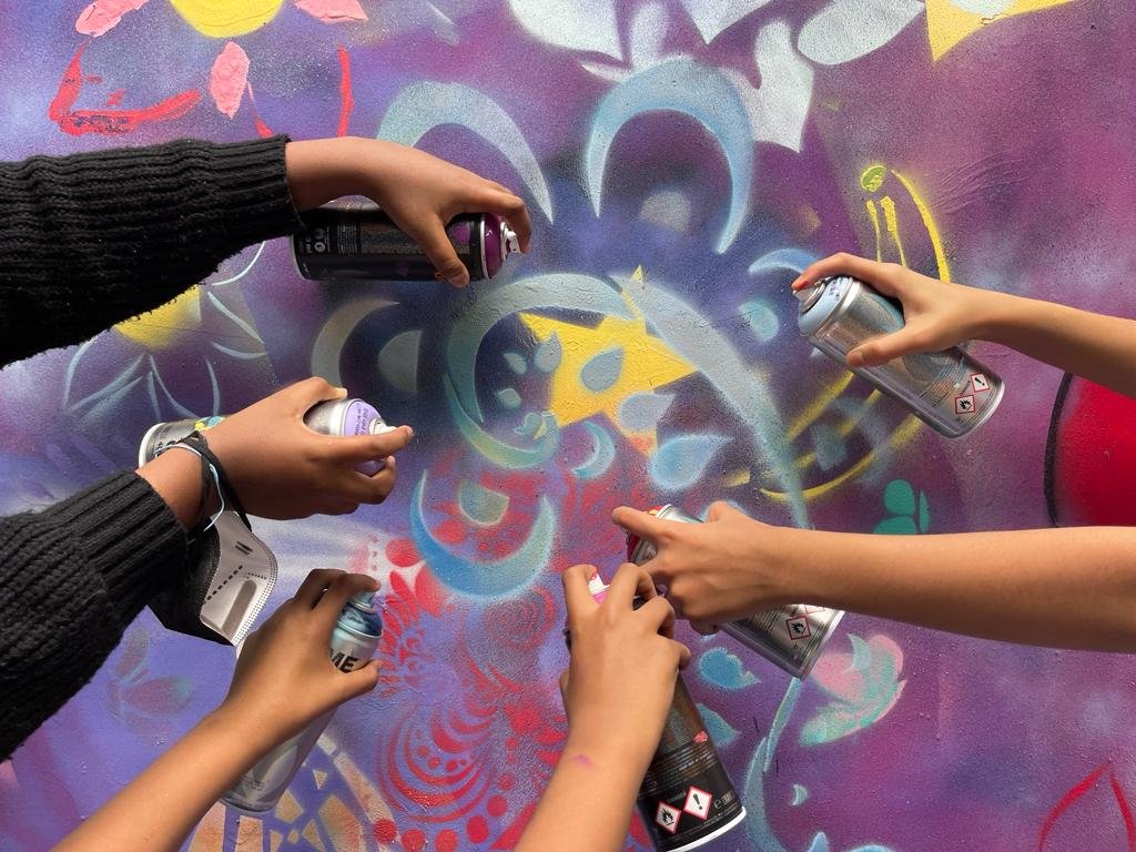 Multiple people spray paint graffiti on a colorful wall with various abstract designs and patterns.