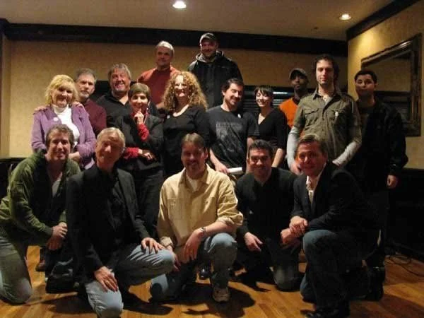 Group of 15 people gathered indoors in a casual setting, posing for a photo.