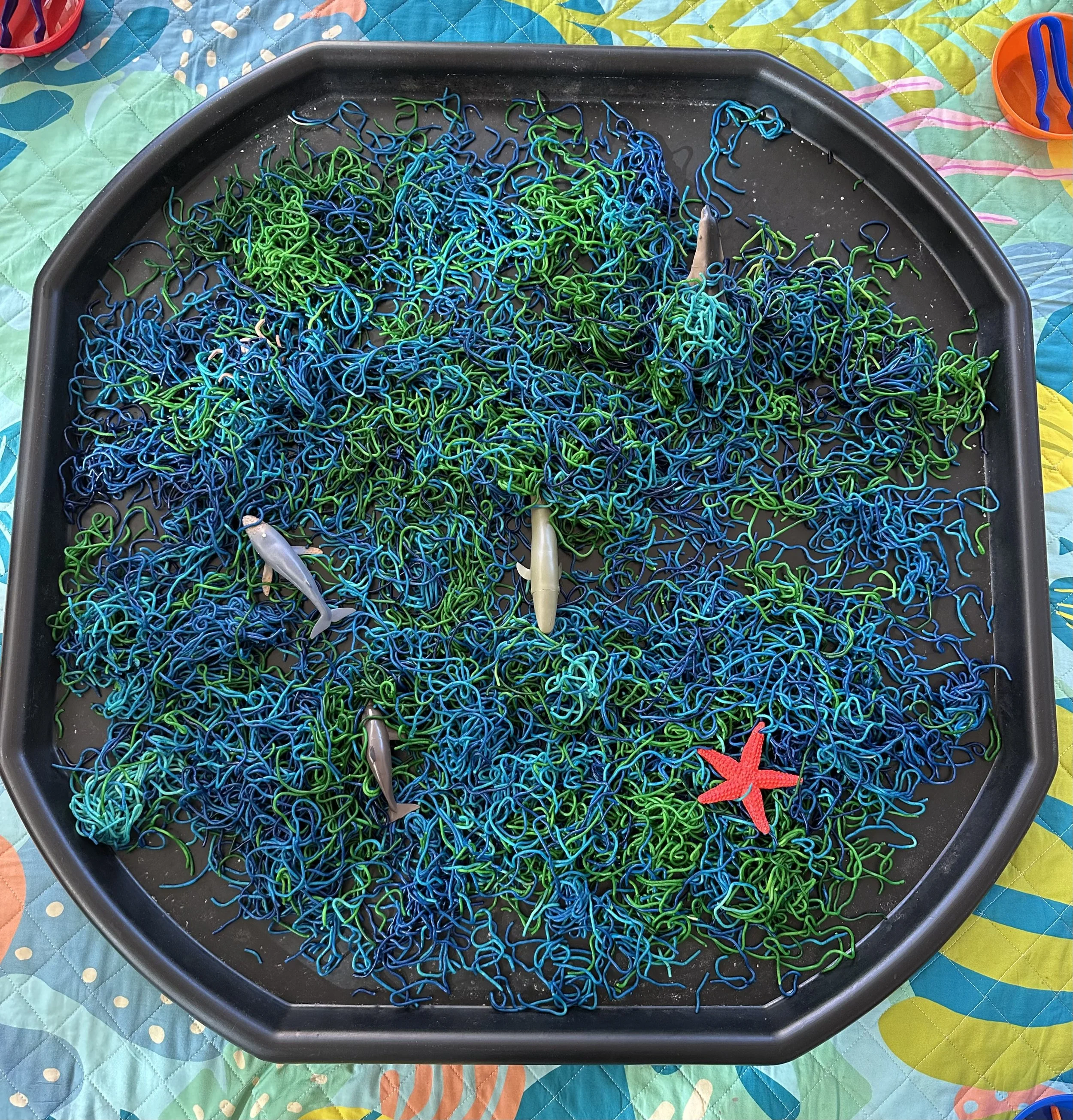 Colorful tangled fishing lines with small fishing lures and a red starfish on top, on a black tray.