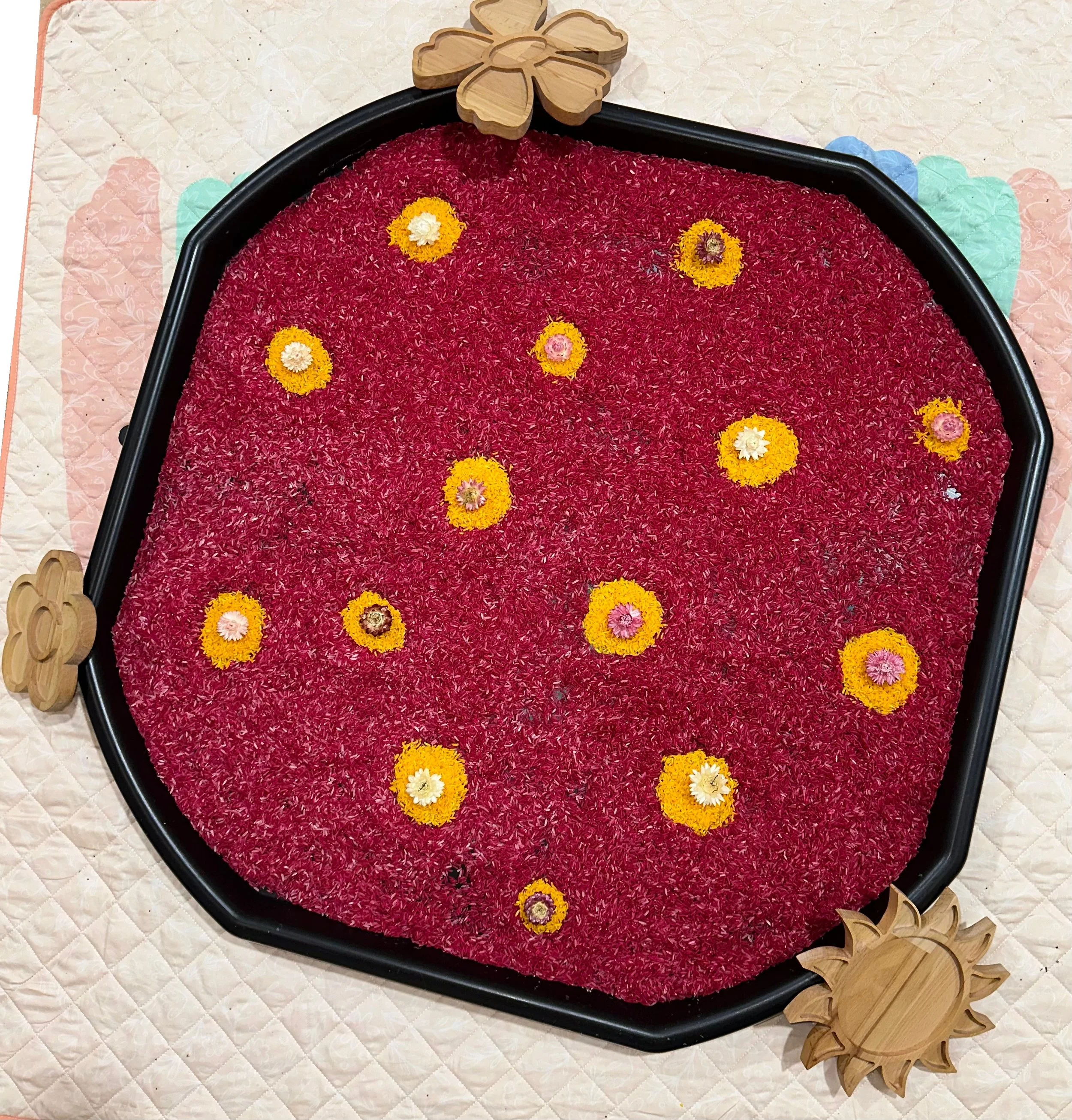 Decorative arrangement resembling a pond with red flower petals, yellow and pink flowers, surrounded by wooden sunflower and flower-shaped accents.