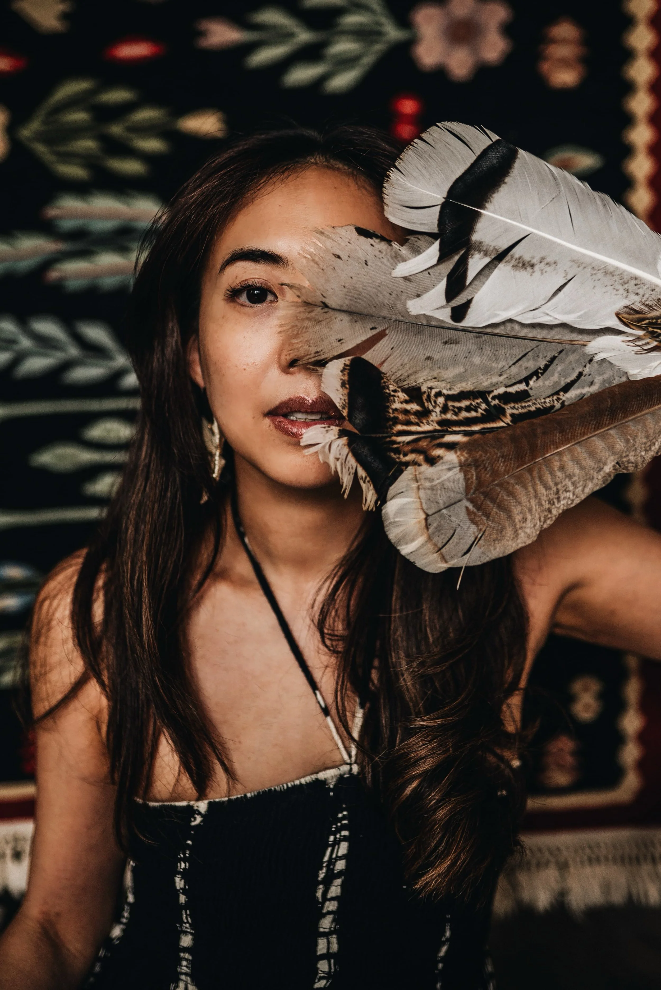a dark-haired woman covering her right eye with a bundle of feathers