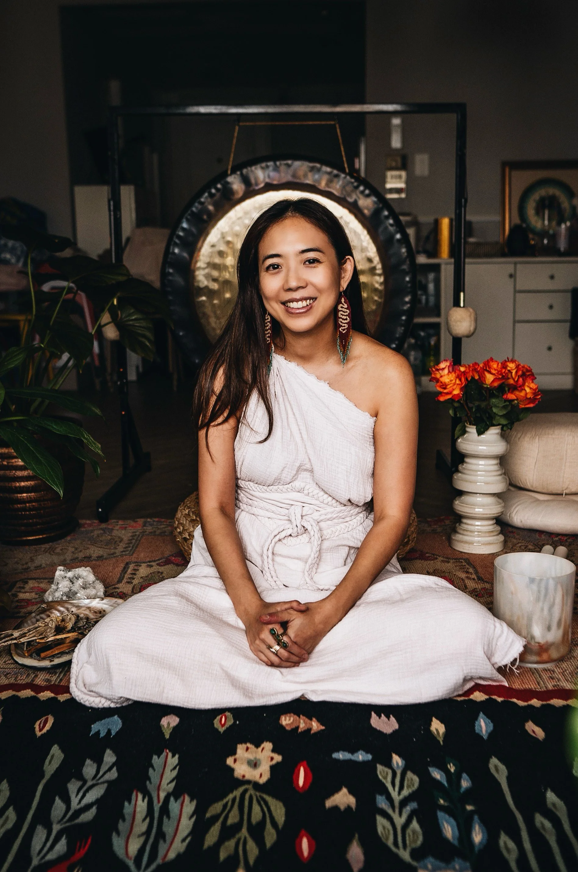 A woman in a beautiful white dress sitting in a sacred space in front of a gong to promote her spiritual workshops and healing sessions in Bangkok