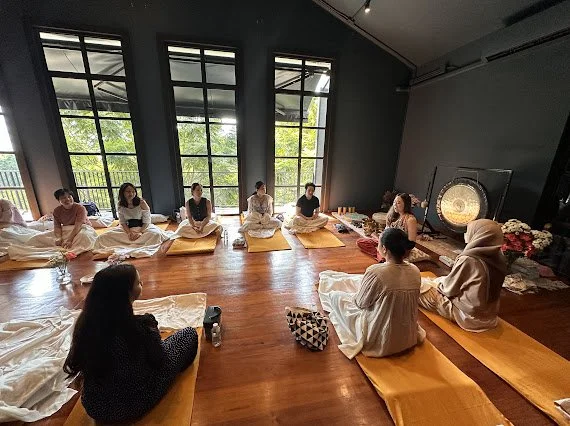 a group of people sitting in a circle on yoga mats in an indoors space, preparing for a reiki training in bangkok, thailand