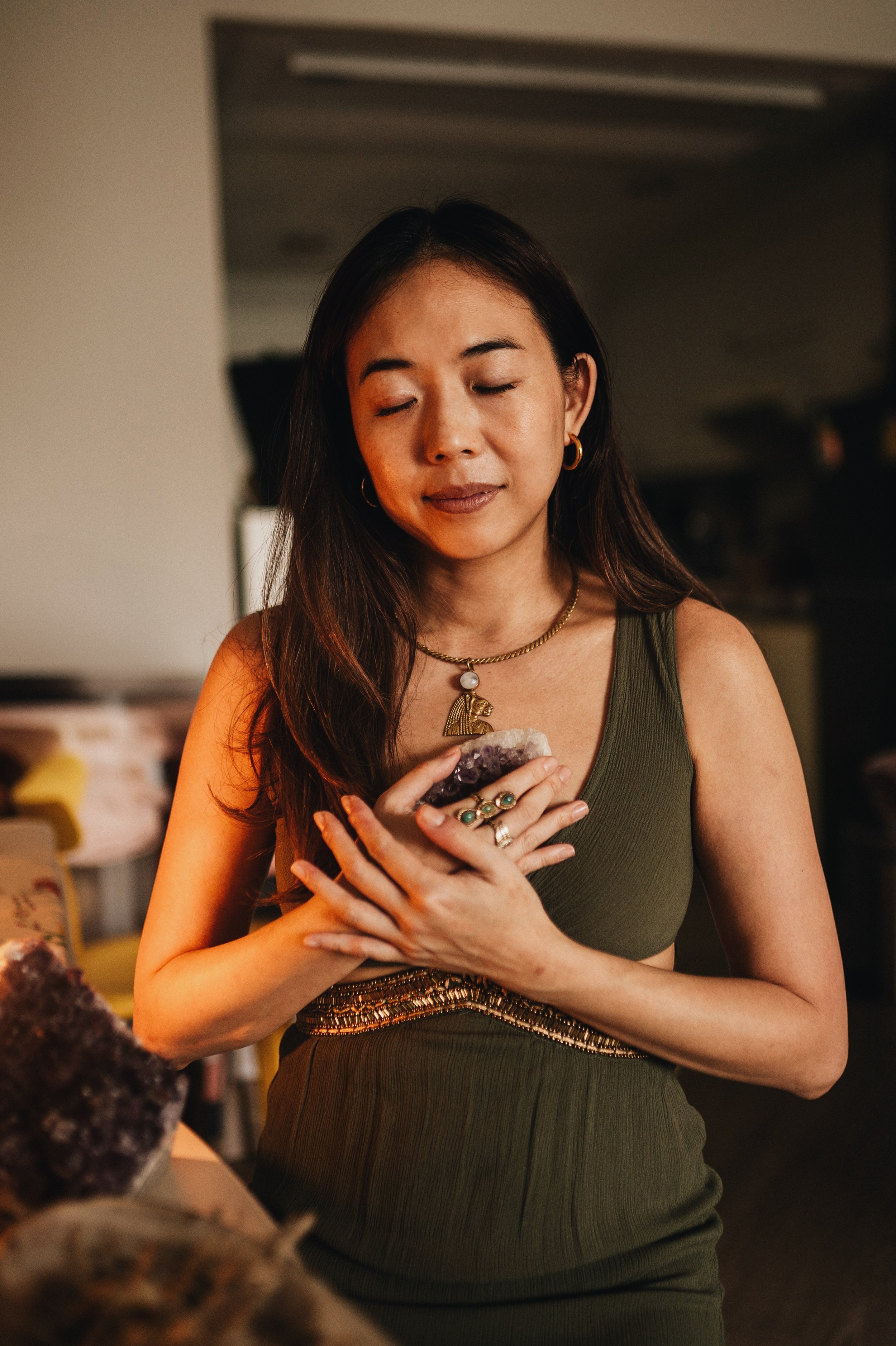 woman with closed eyes and sacred jewelry holding an amethyst crystal on her heart, illustrating a crystal healing course in bangkok thailand.