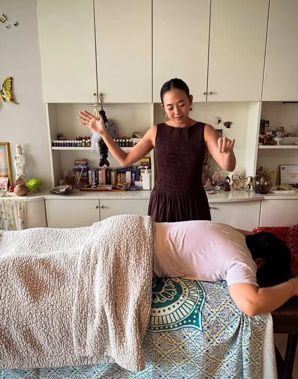 a woman performing a spinal energetics session in a sacred space in bangkok thailand, on a client that is laying down on a massage table
