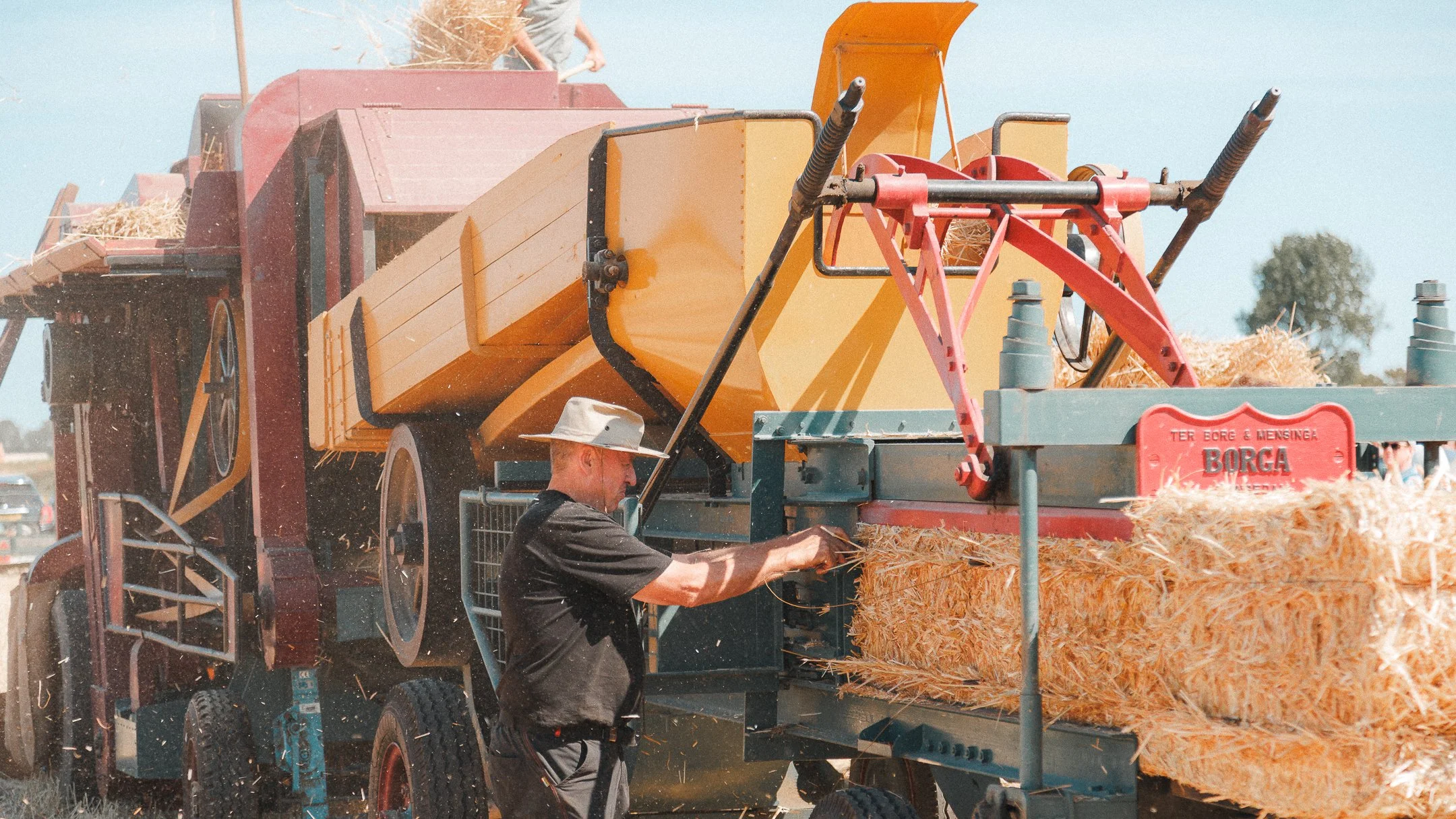 Man met hoed die stro uit een machine haalt tijdens graanverwerking op een boerenbedrijf.