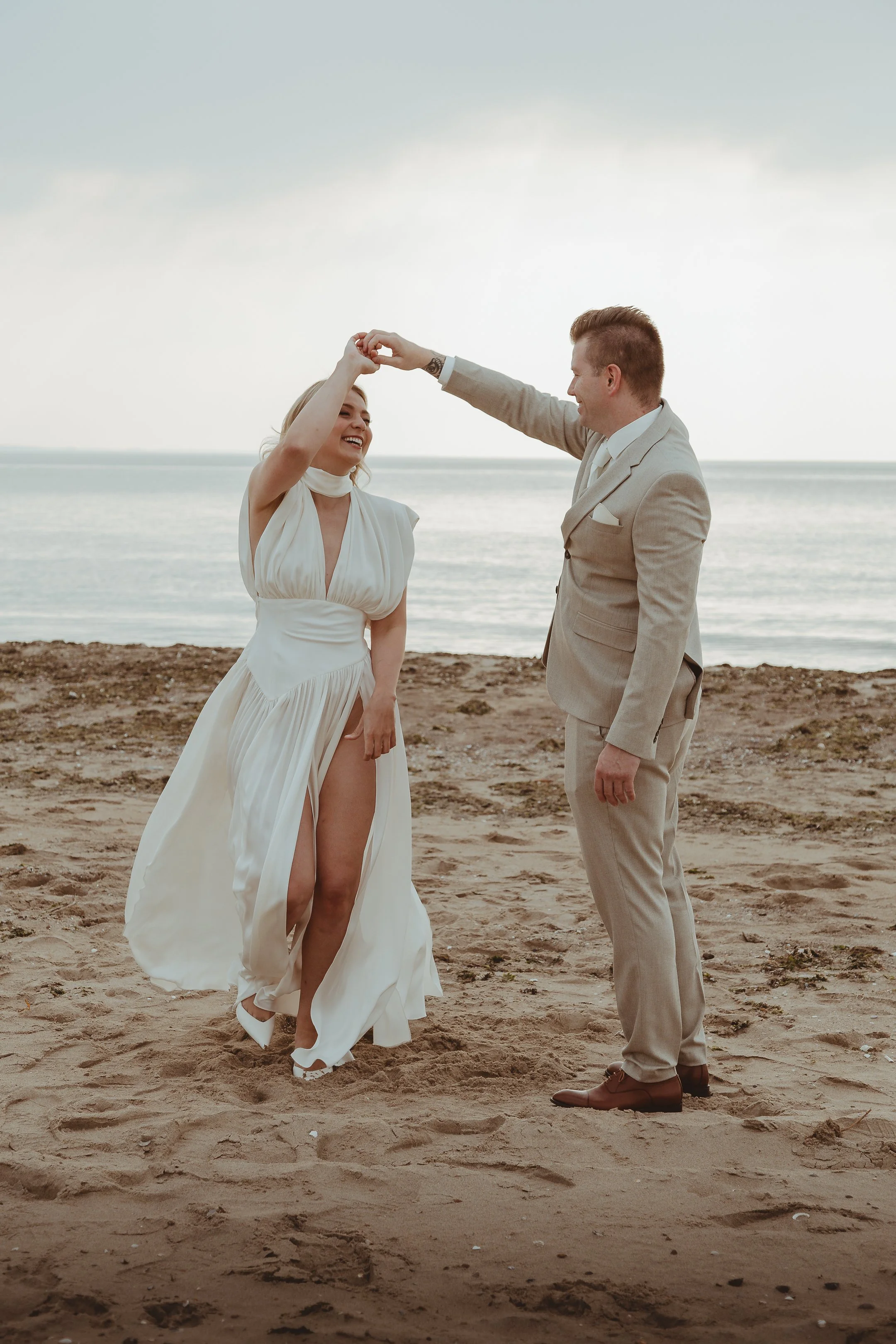 Een paar dat op het strand trouwt, met de man die de vrouw hand vasthoudt en haar als ze danst.