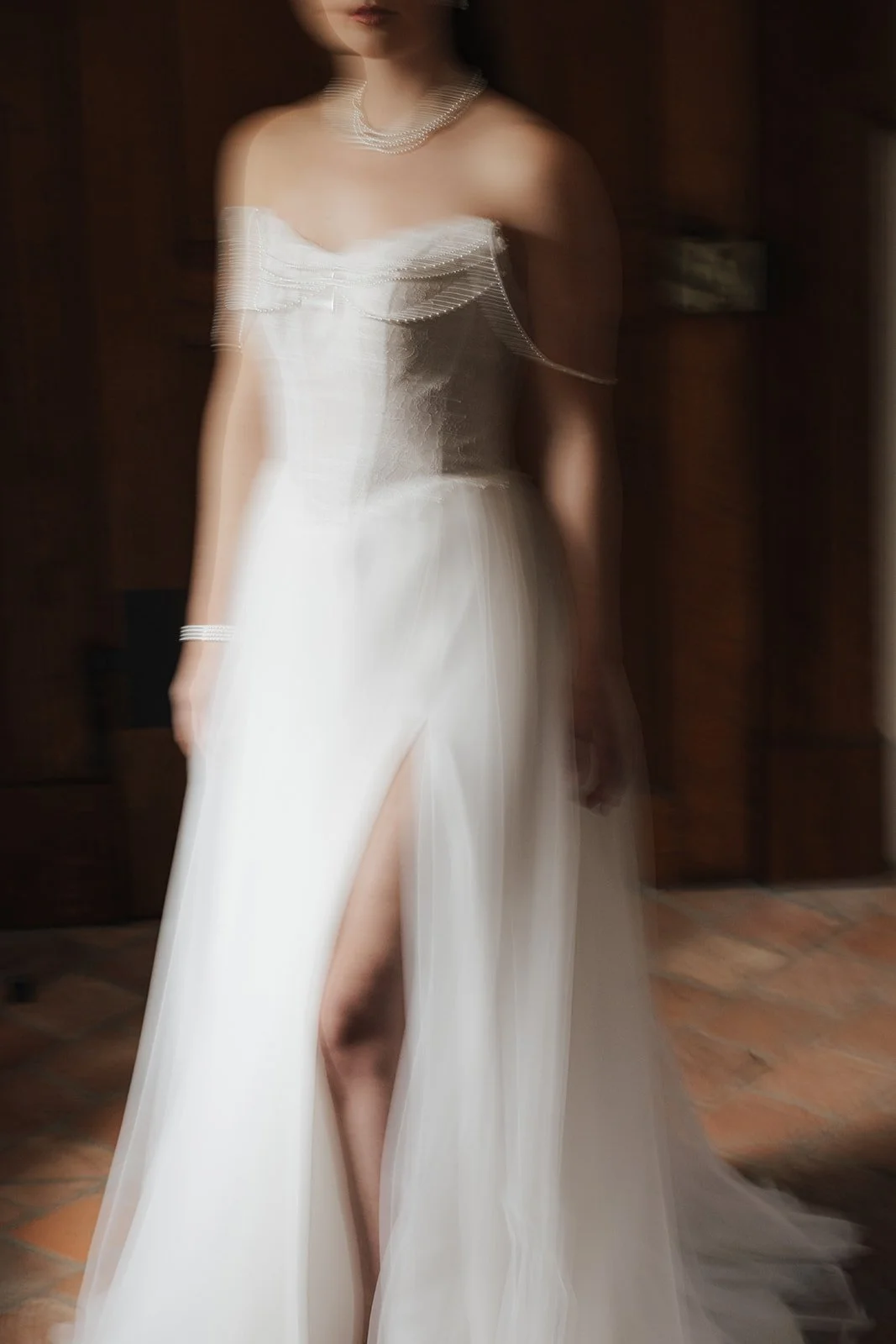 Eine Frau in einem weißen Brautkleid mit hohem Beinschlitz, die Schmuck trägt, steht in einem Raum mit Holzvertäfelung.