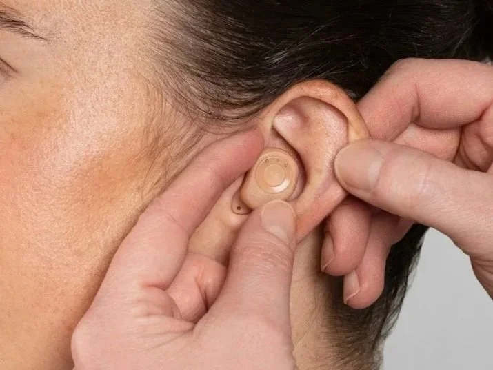 Person placing a behind-the-ear hearing aid in their ear.